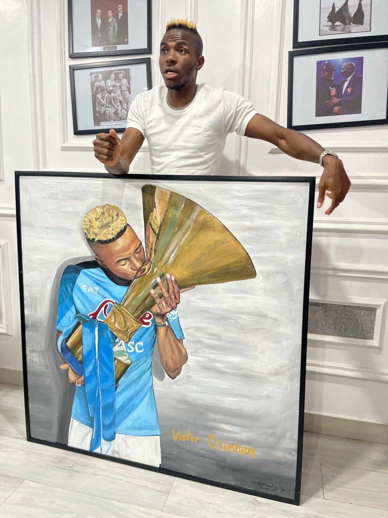 Person standing behind a framed caricature of a football player holding a trophy, in an art gallery.