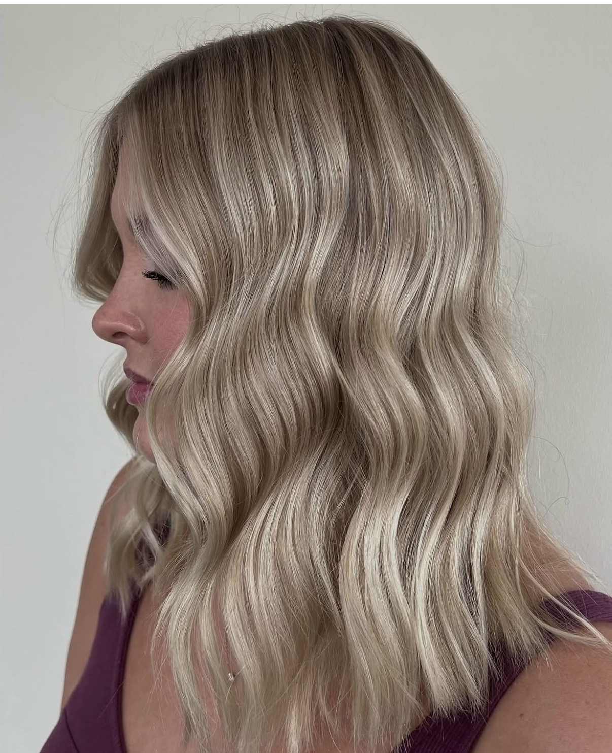 Side view of a woman with wavy, blonde hair and a purple top, facing left.