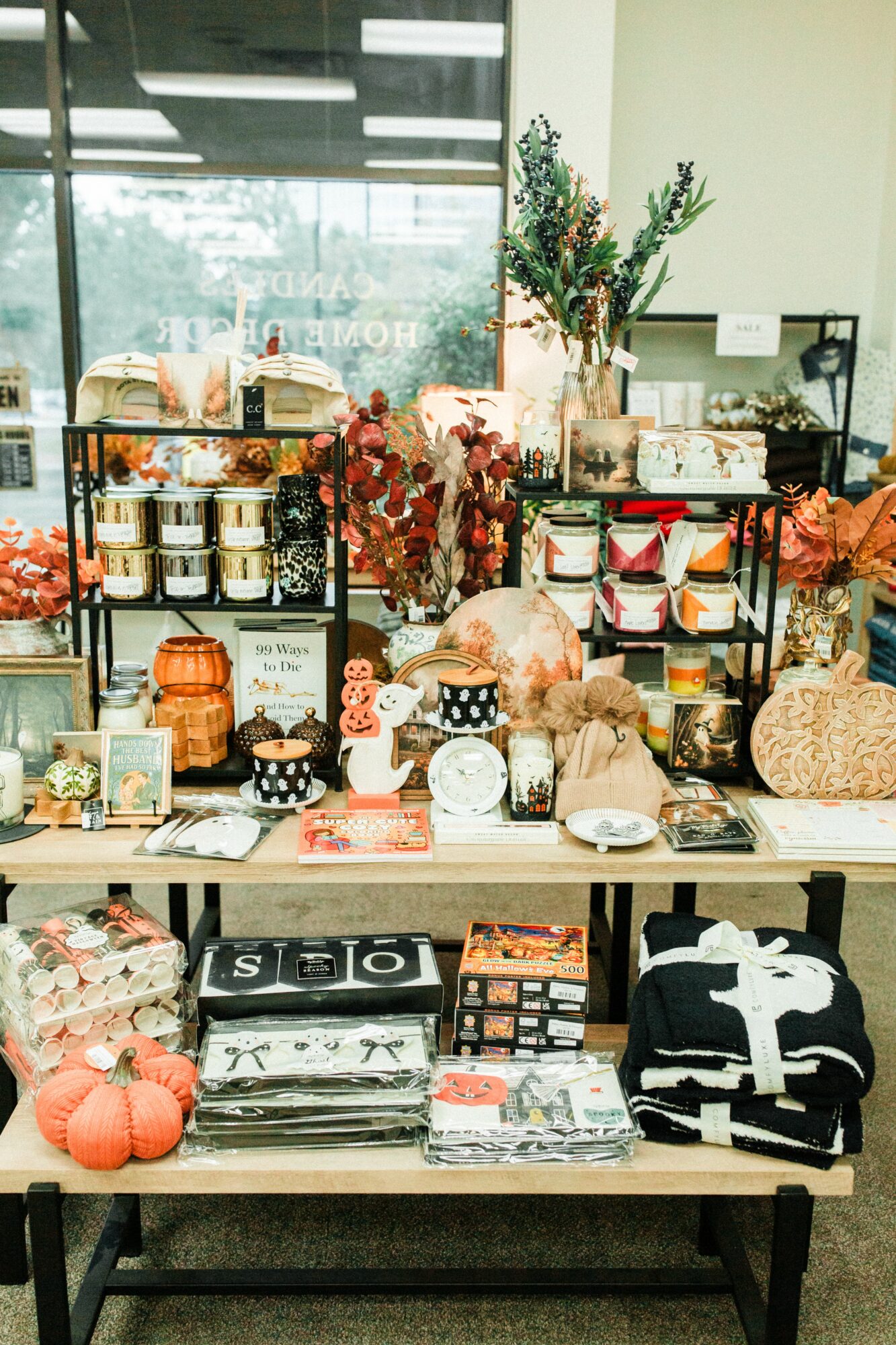 Display of various decorative items, including flowers, candles, and small containers, arranged on a table inside a store with a large window.
