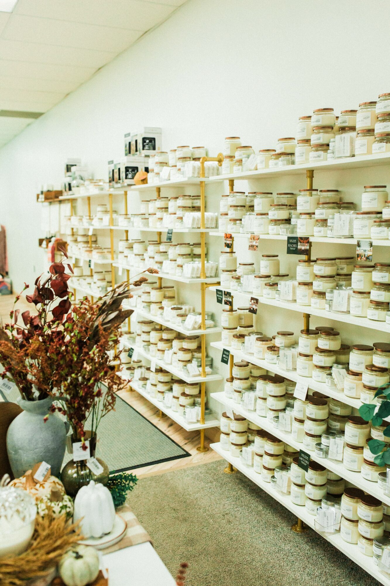 Shelves filled with small containers in a store, with a table of decorative items and flowers in the foreground.