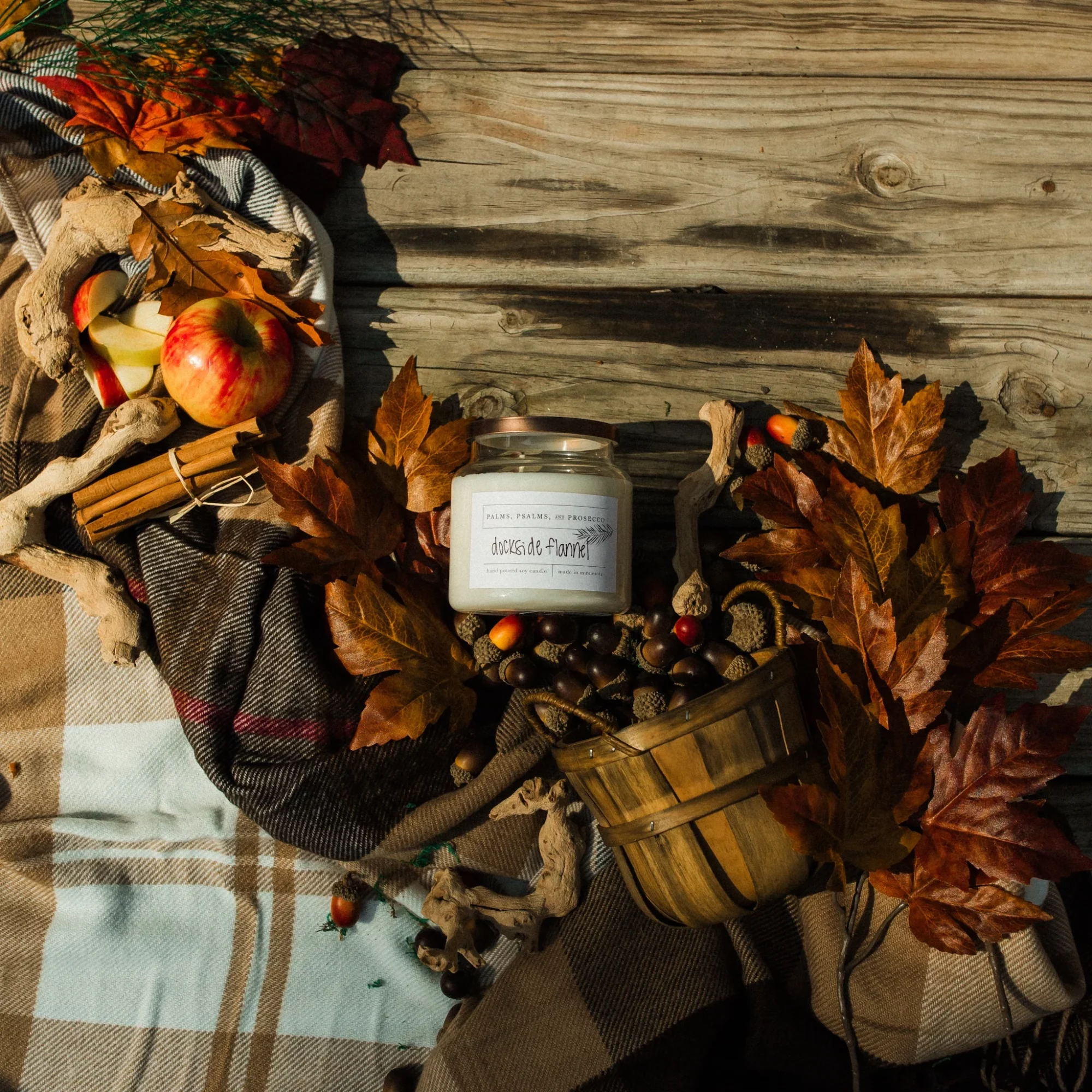 Autumn-themed arrangement with leaves, apples, and a candle on a wooden surface, with fabric and decorative items.