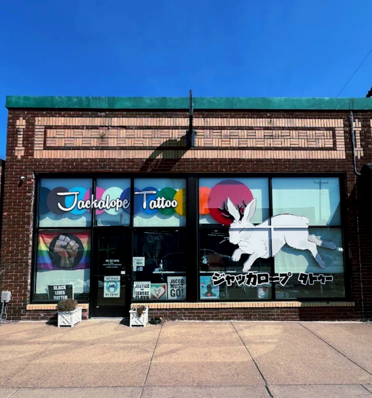 Storefront with large window display featuring a white unicorn, Japanese text, and colorful signs, under a brick building with a green roof.