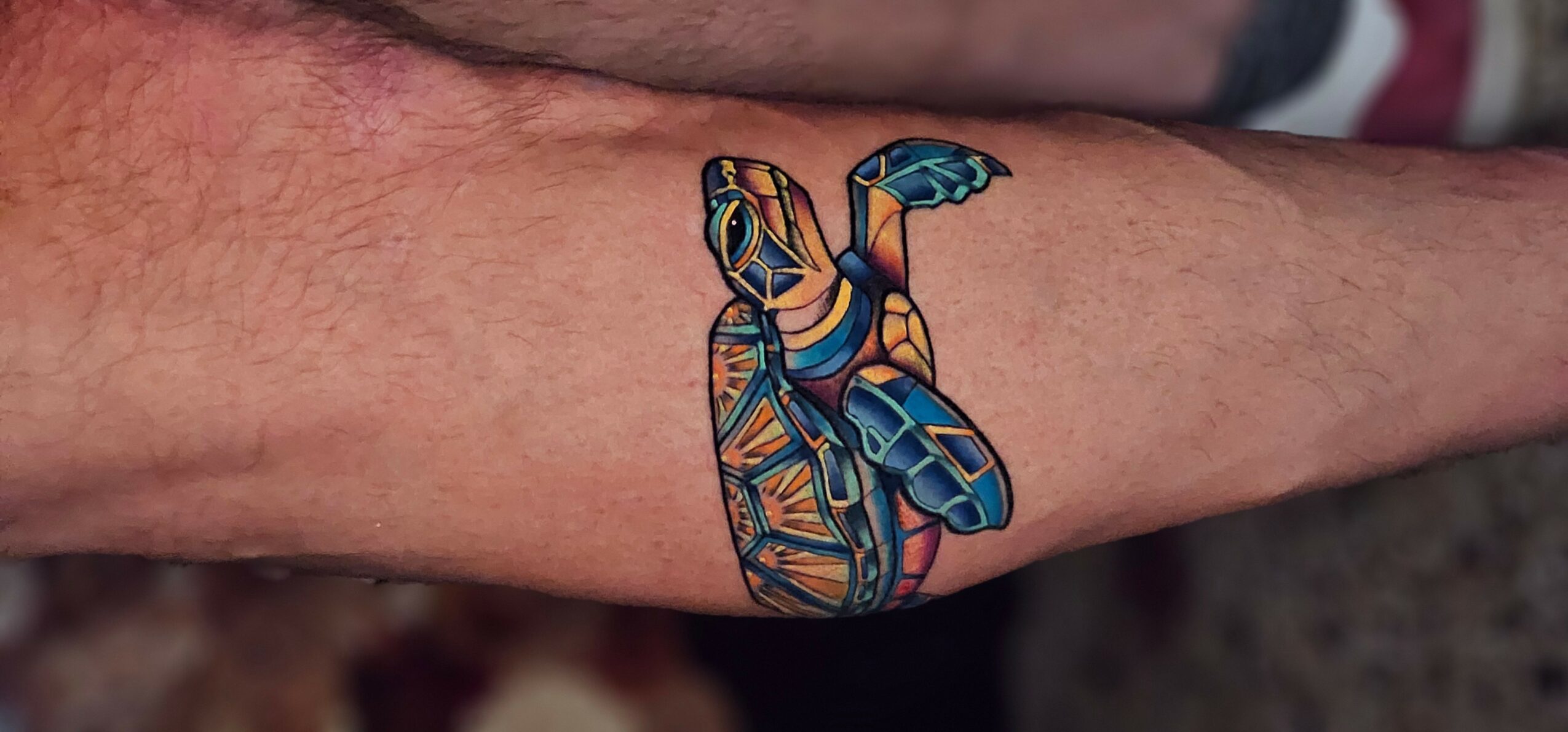 Colorful tattoo of a stylized insect on skin, with intricate line work and vibrant shades of blue, orange, and yellow.
