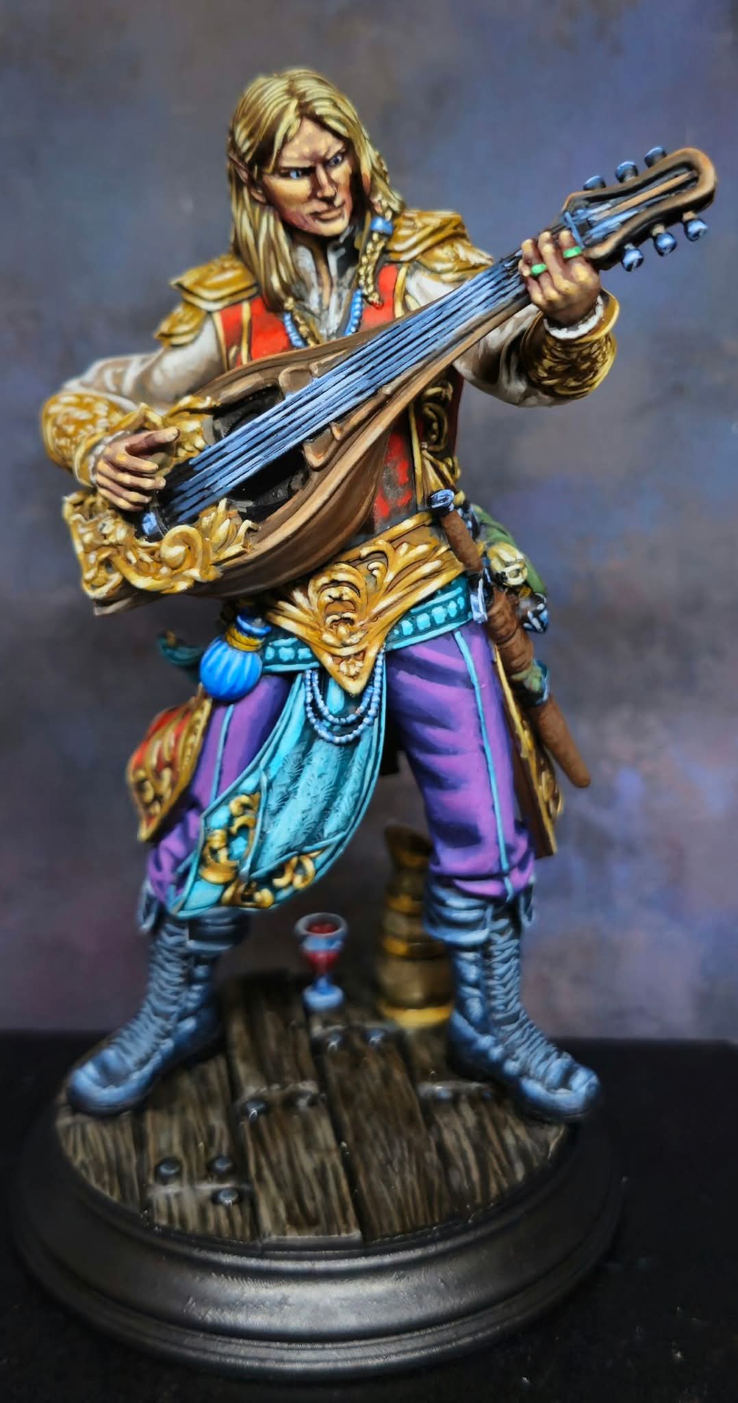 Figurine of a person in colorful clothing playing a stringed instrument, standing on a wooden base.