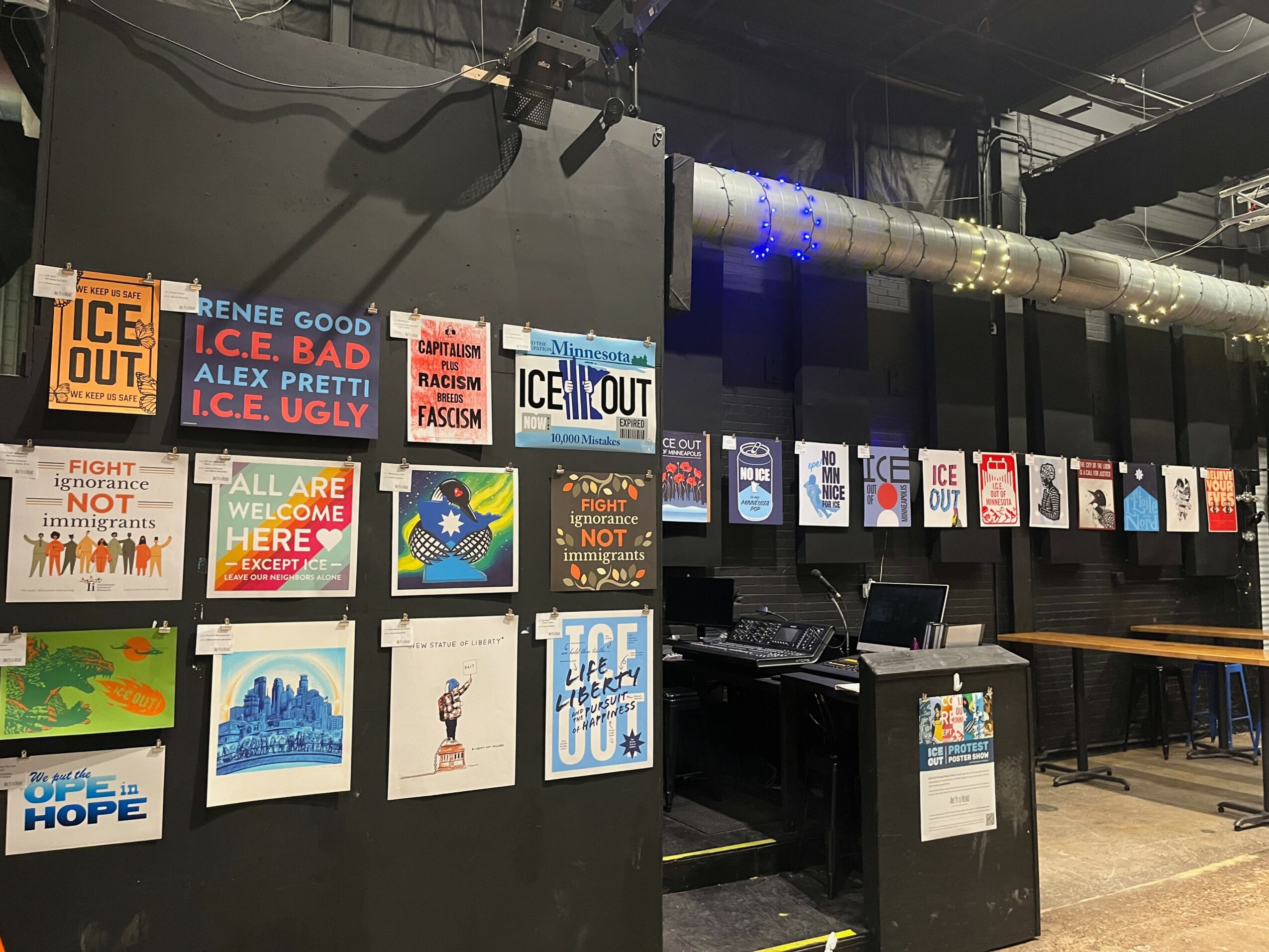 Wall with various colorful posters and signs, some with text, in an indoor setting with pipes and equipment visible.