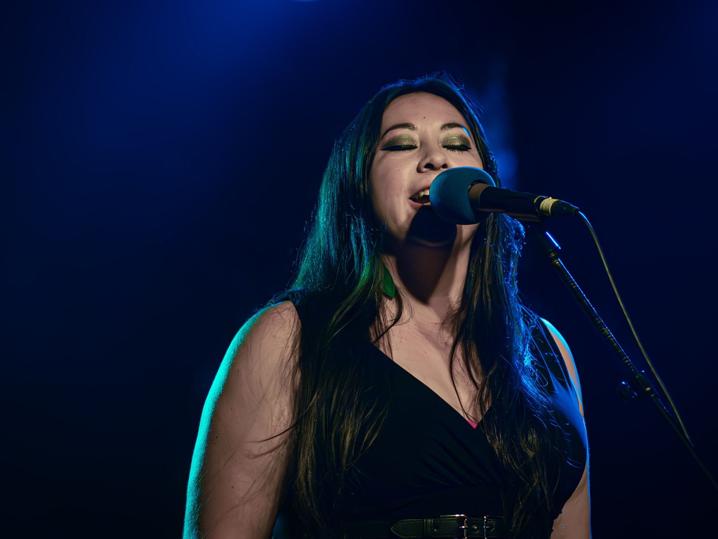 Woman singing into a microphone on stage with dark background and blue lighting