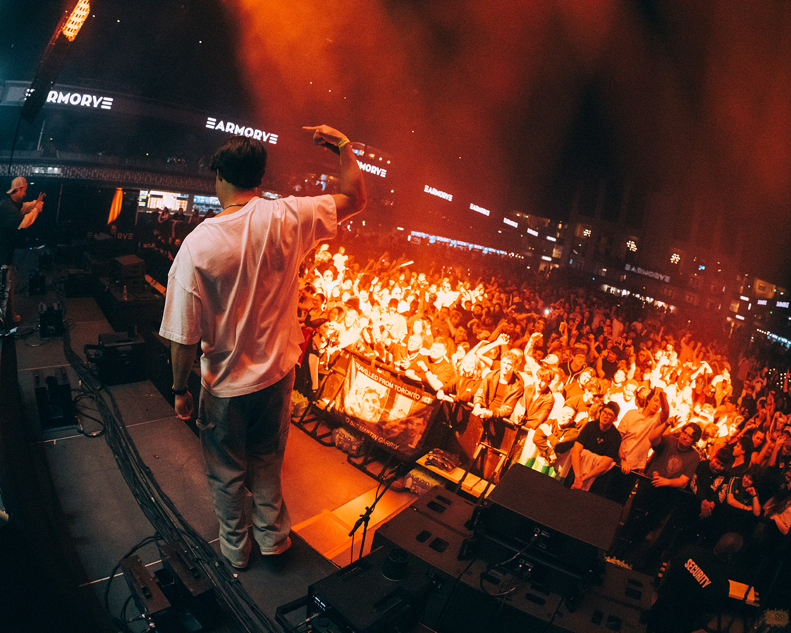 DJ performing on stage with a crowd and bright lights in the background.