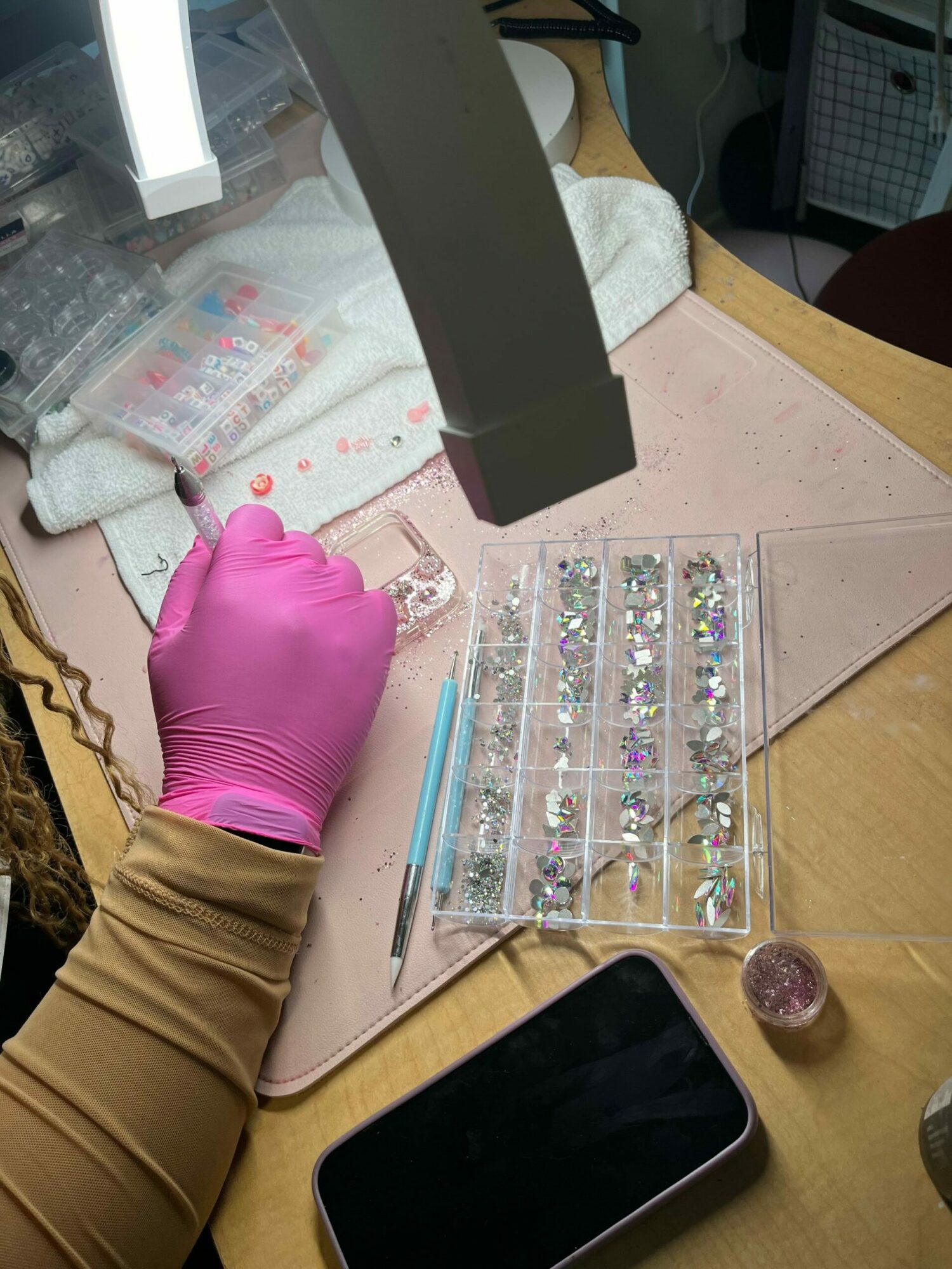 Person wearing pink glove handles small objects in a plastic container on a table with a smartphone and tools.