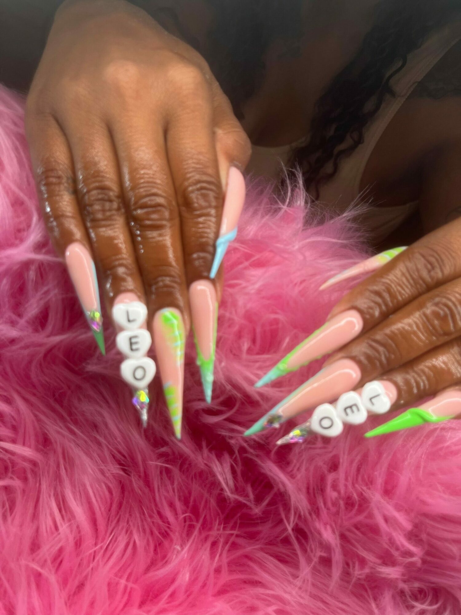 Close-up of hands with long, colorful, decorated nails resting on pink fluffy material.