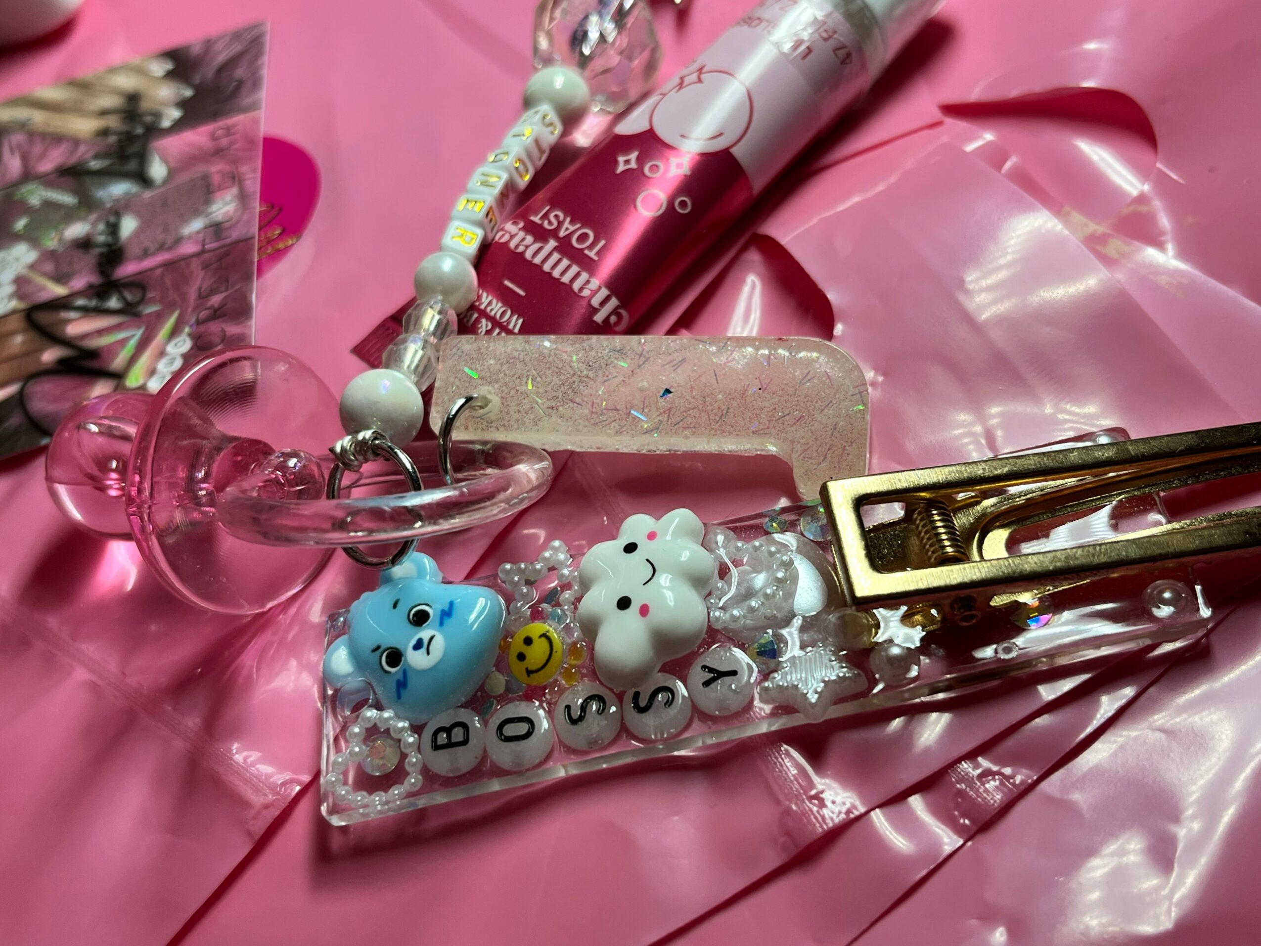 Pink background with hair clips, beads, and a butterfly sticker, featuring a small decorated surface with letters and animal figures.