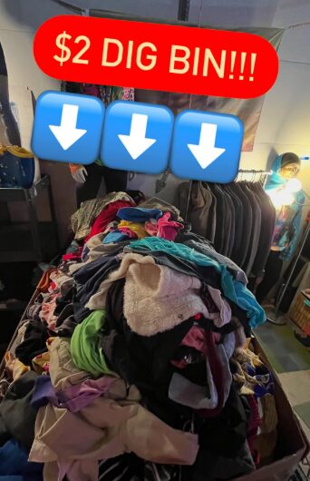 Pile of clothes with a red sign reading '$2 DIG BIN!!!' above, in a store setting.