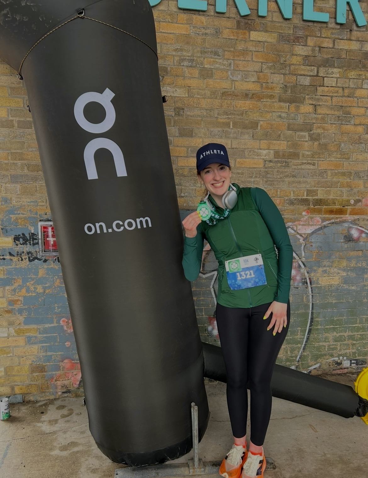 Young woman in athletic clothing and a cap, smiling, standing next to a large black punching bag outdoors.