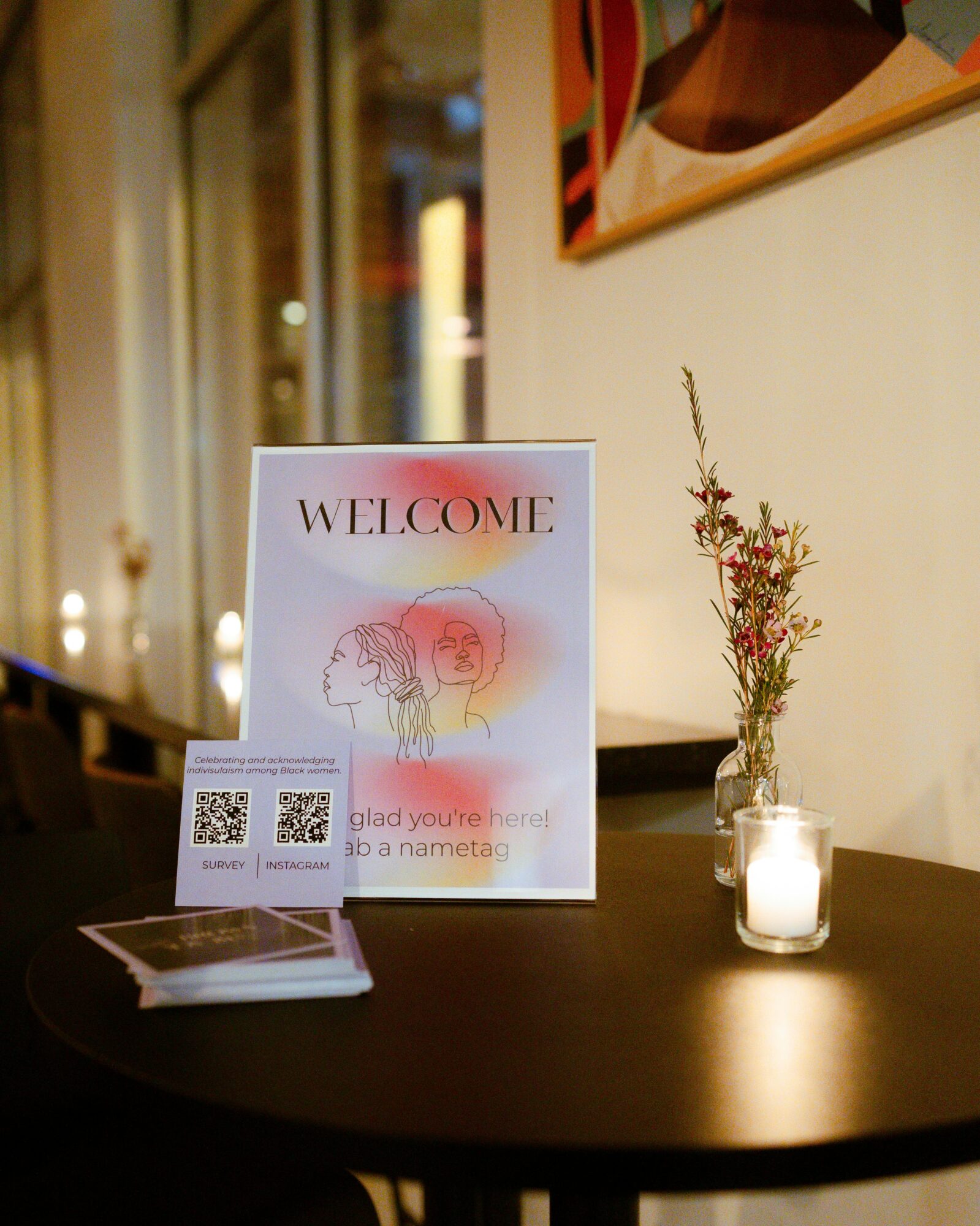 Welcome sign on table with QR codes, a small vase with flowers, and a lit candle in a glass holder.