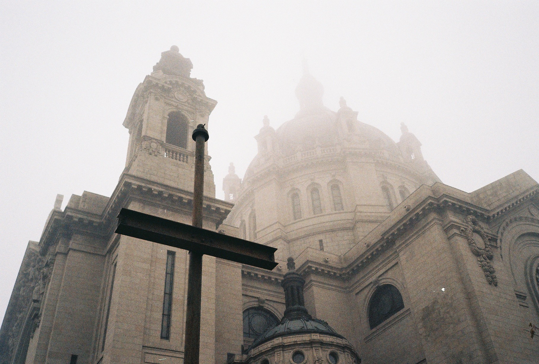 A historic building with domes and towers, viewed from below, shrouded in fog or mist.