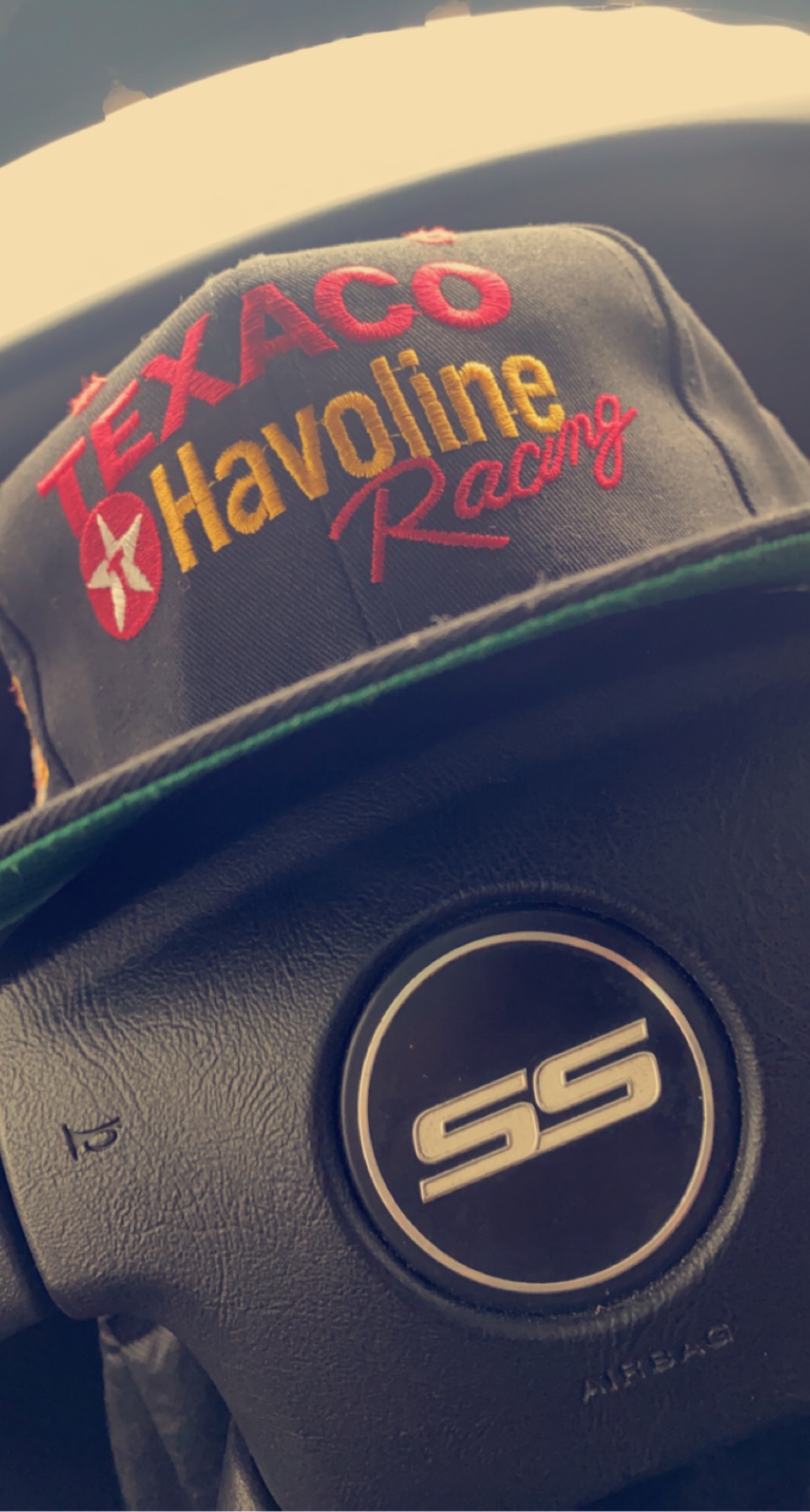 Cap with Texaco Havoline Racing logo placed on a steering wheel, close-up view.