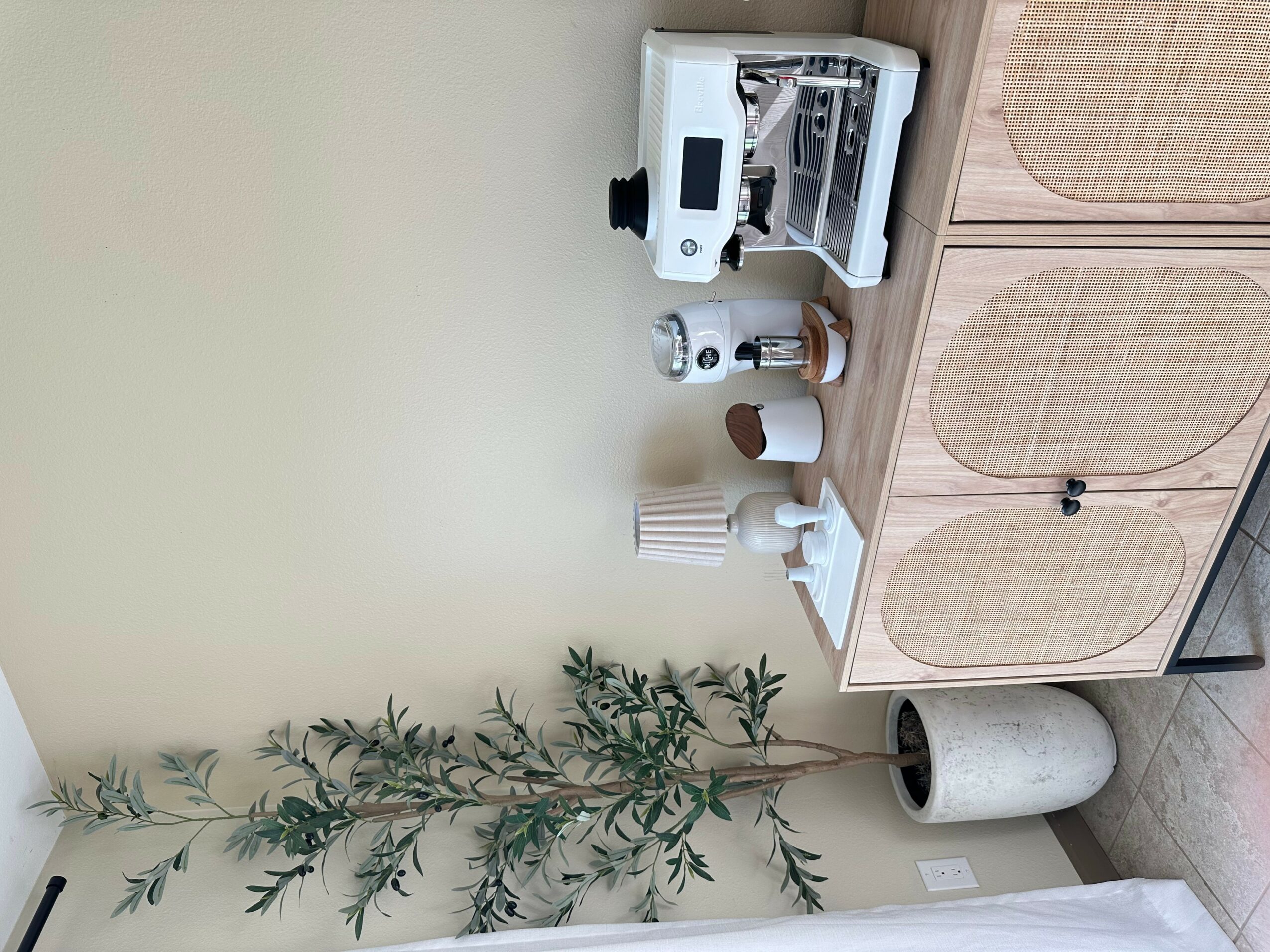 Coffee machine, cups, and a plant on a wooden cabinet against a light-colored wall.