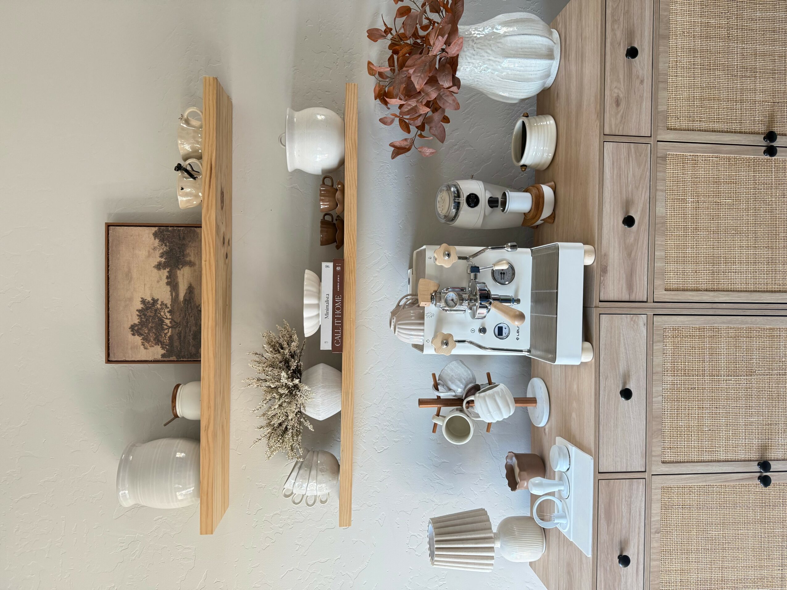 Decorative shelves with vases, plants, and art pieces on a wall, with a table holding various objects below.