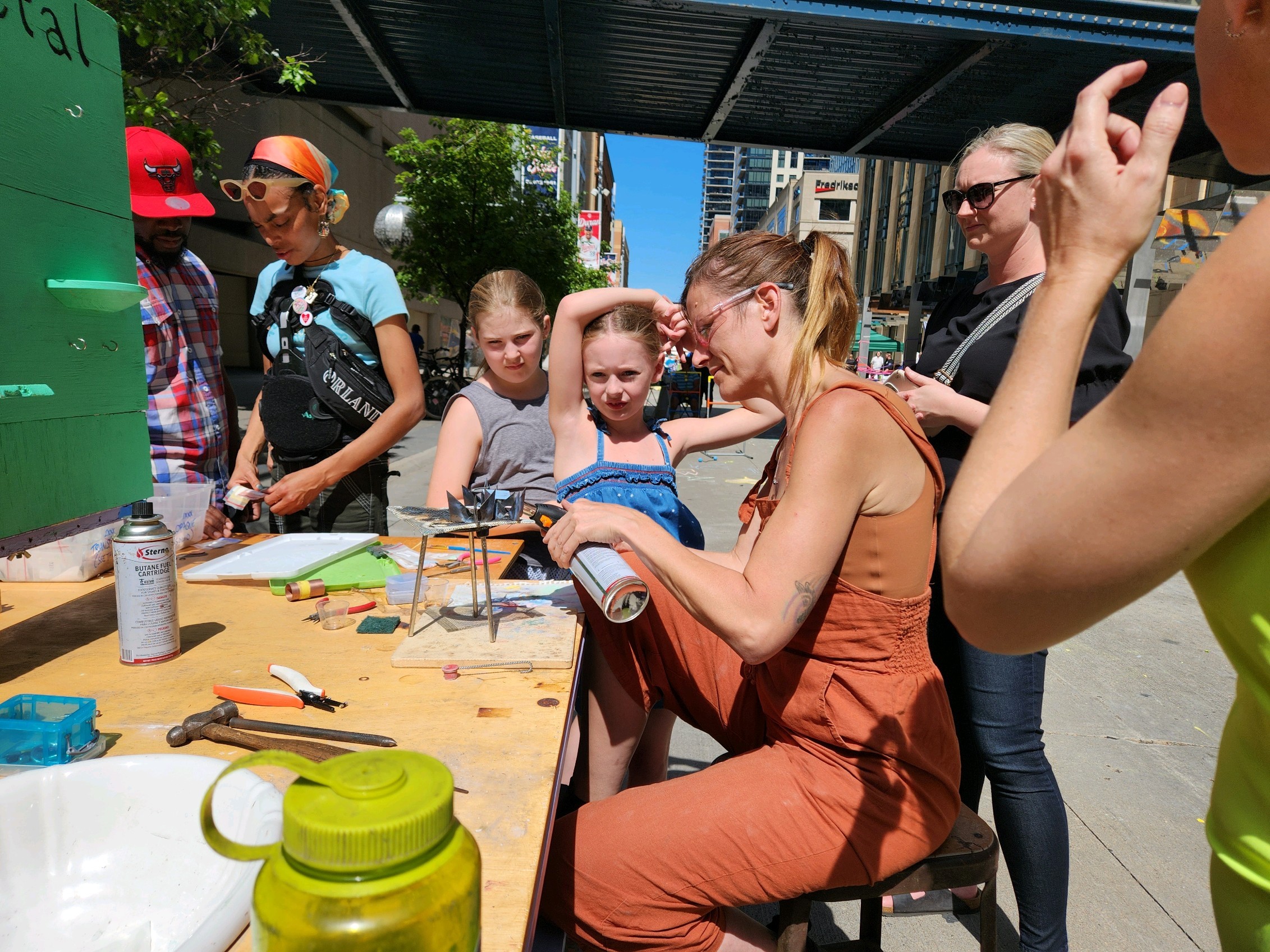 Group of children and adults around a table outdoors, engaging in arts and crafts activities.