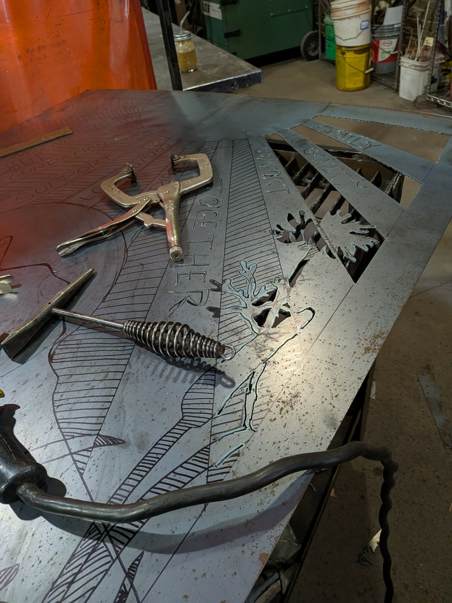 Metalwork workshop with tools and a partially cut decorative metal sheet on a workbench.