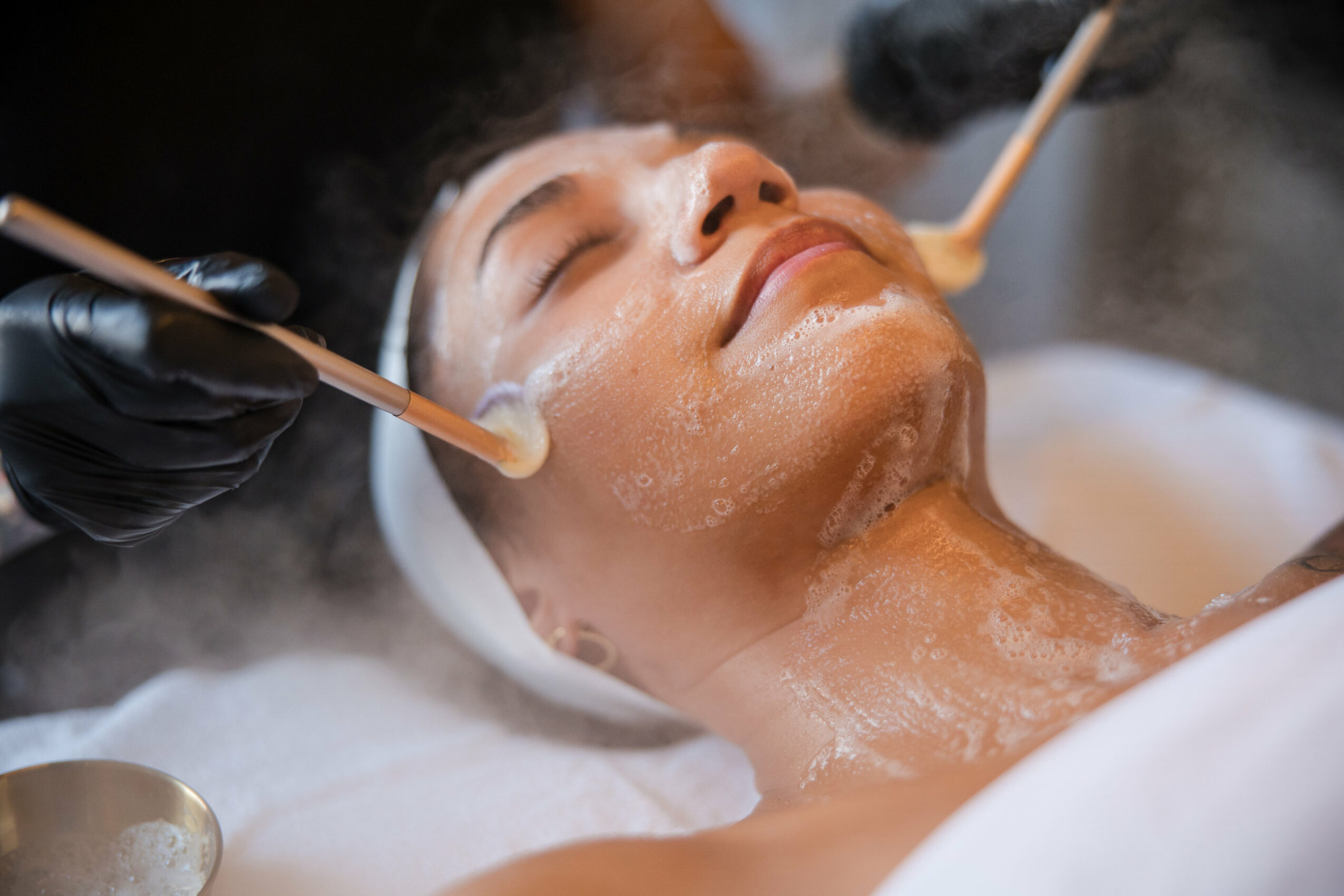 Woman receiving facial treatment with tools, lying with eyes closed, in a spa setting.