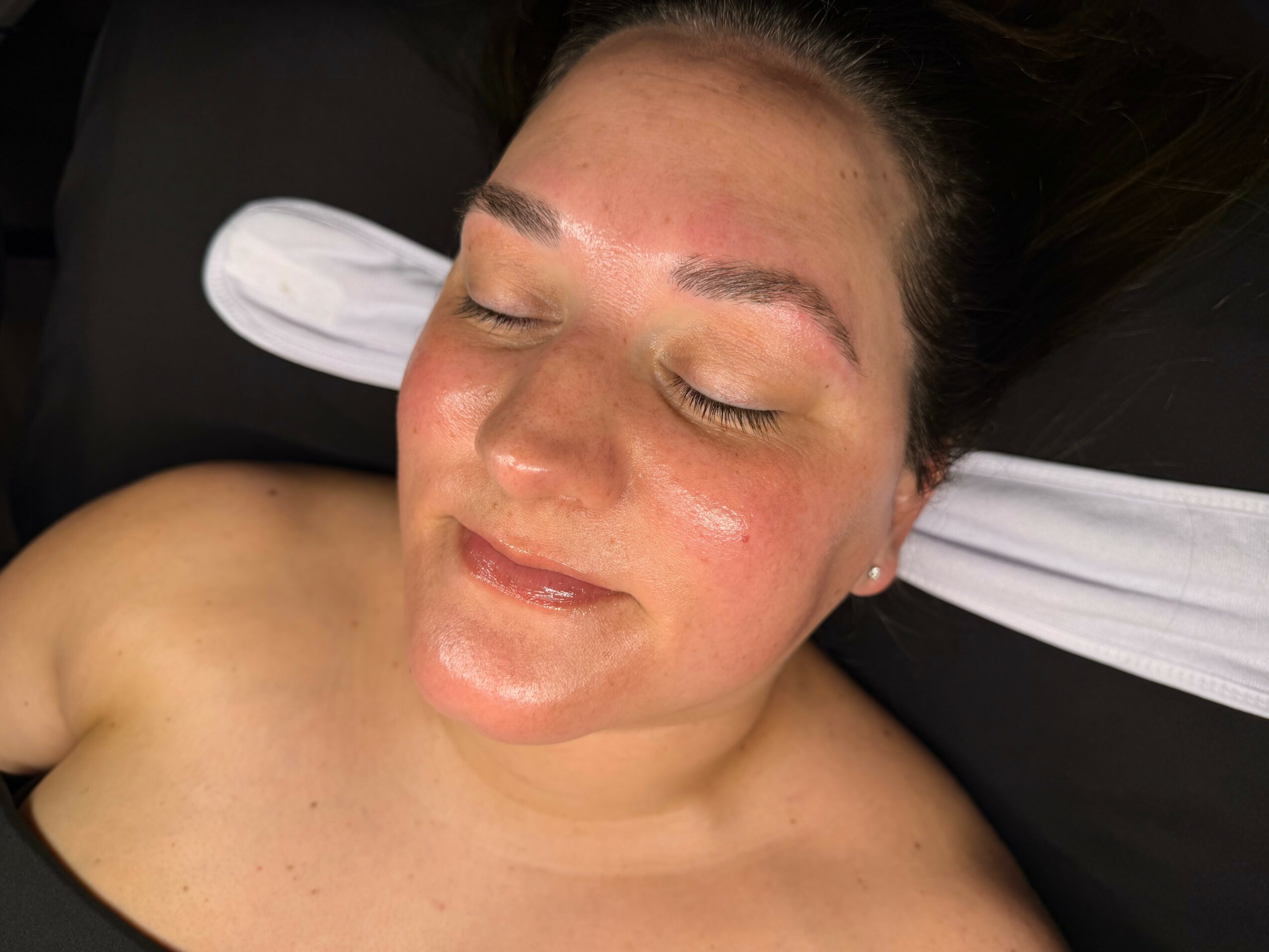 Close-up of a woman with closed eyes and a relaxed expression, lying down with a pillow behind her head.