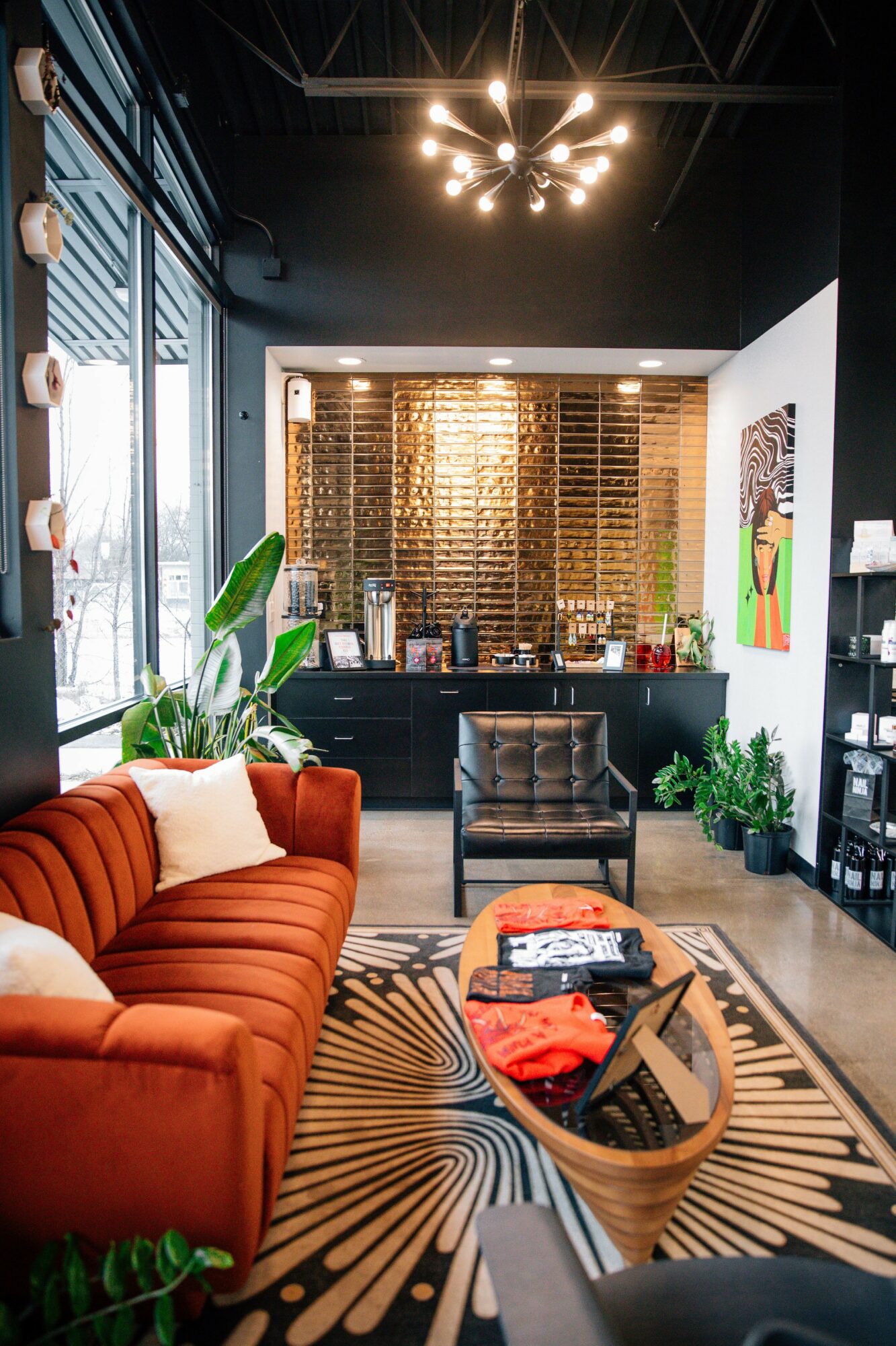 Living room with orange sofa, black armchair, coffee table, and plants, with a bar area in the background and modern lighting.