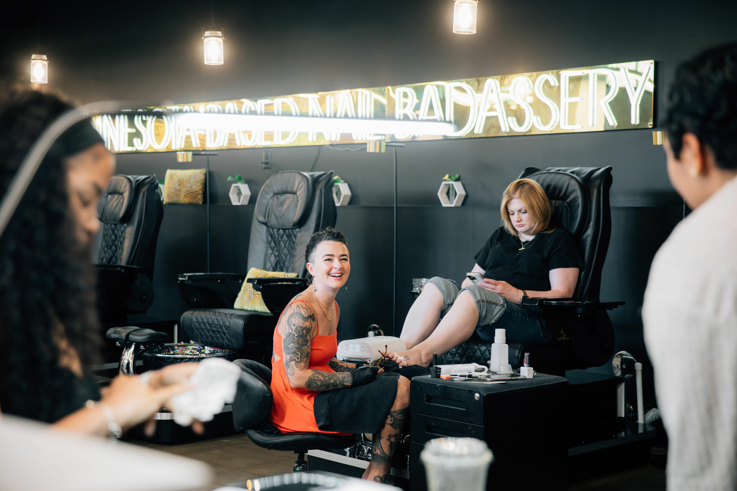 People getting pedicures at a salon, with one woman smiling and another relaxing in a chair.