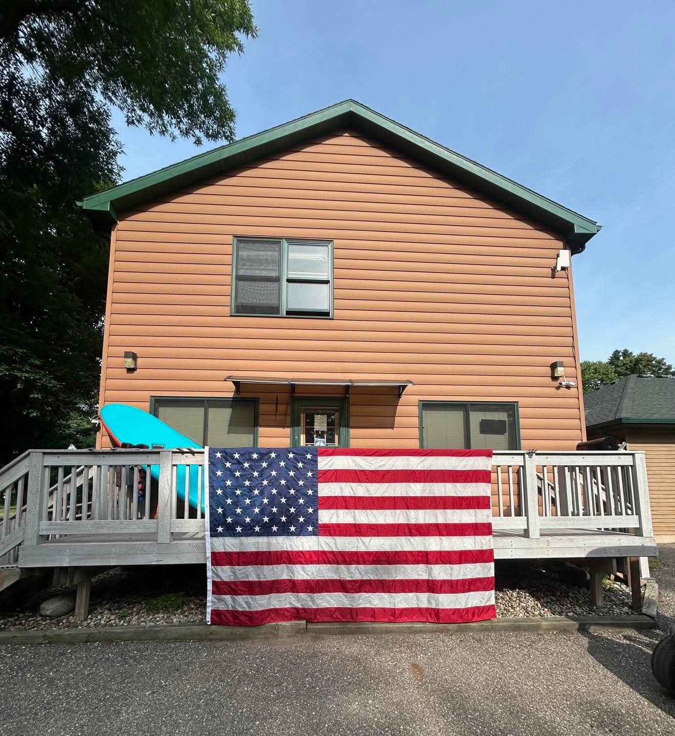 Two-story house with peach siding, green roof, and a deck with an American flag hanging over the railing.
