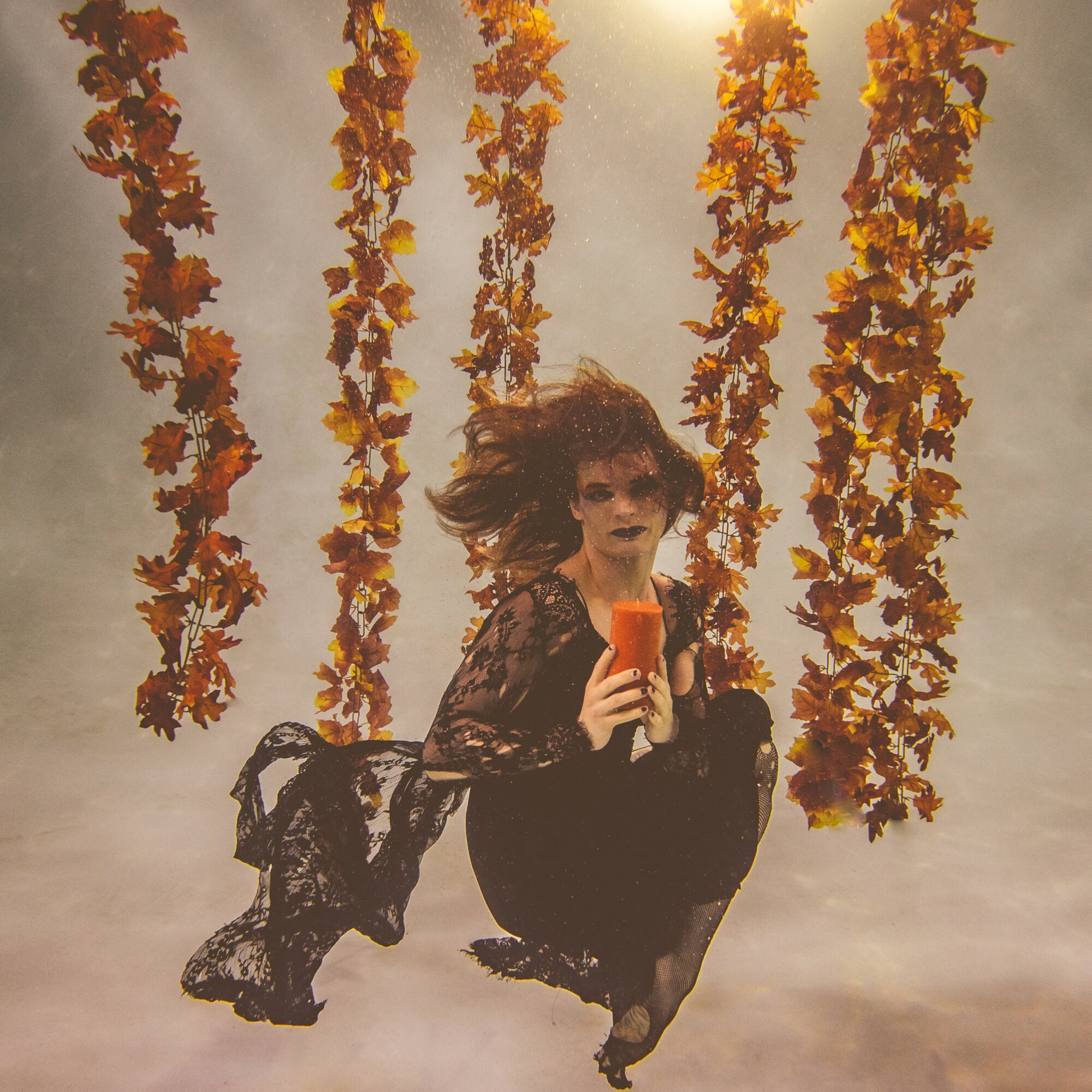 Person with curly hair taking a selfie, surrounded by hanging orange flowers, against a cloudy sky background.