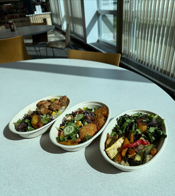 Three oval dishes with salads and fried items on a round table in a bright room with large windows