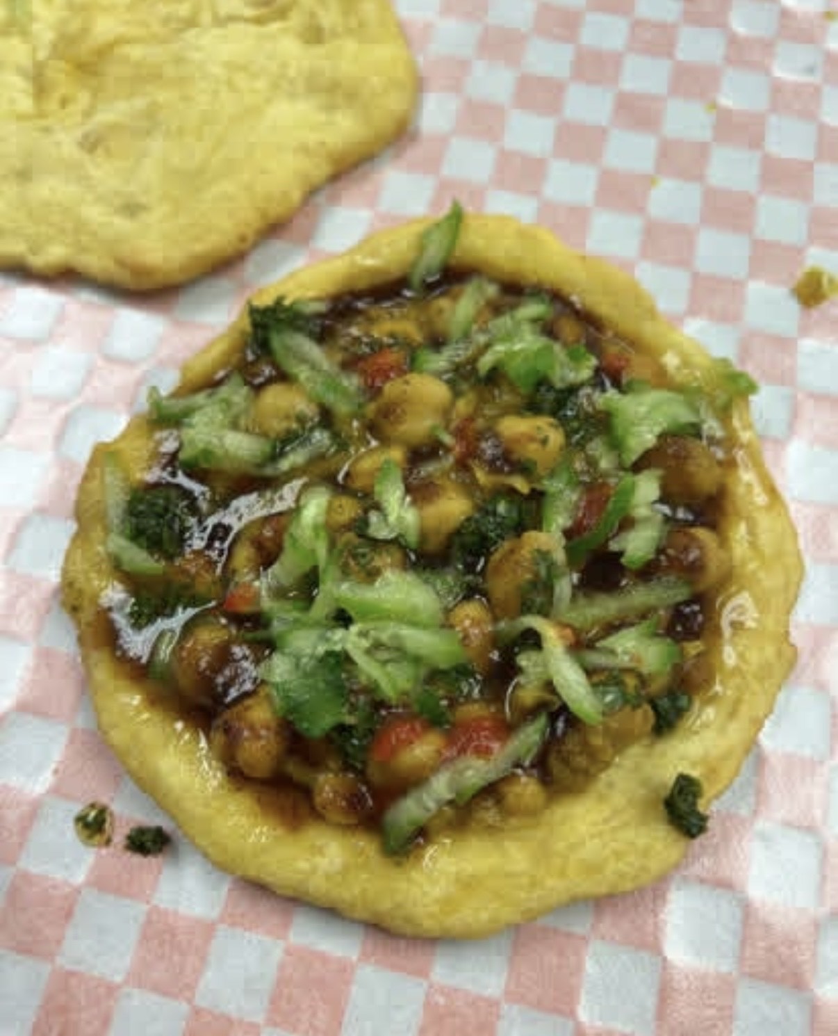 Vegetarian taco with beans, lettuce, and sauce on a checkered paper, viewed from above.