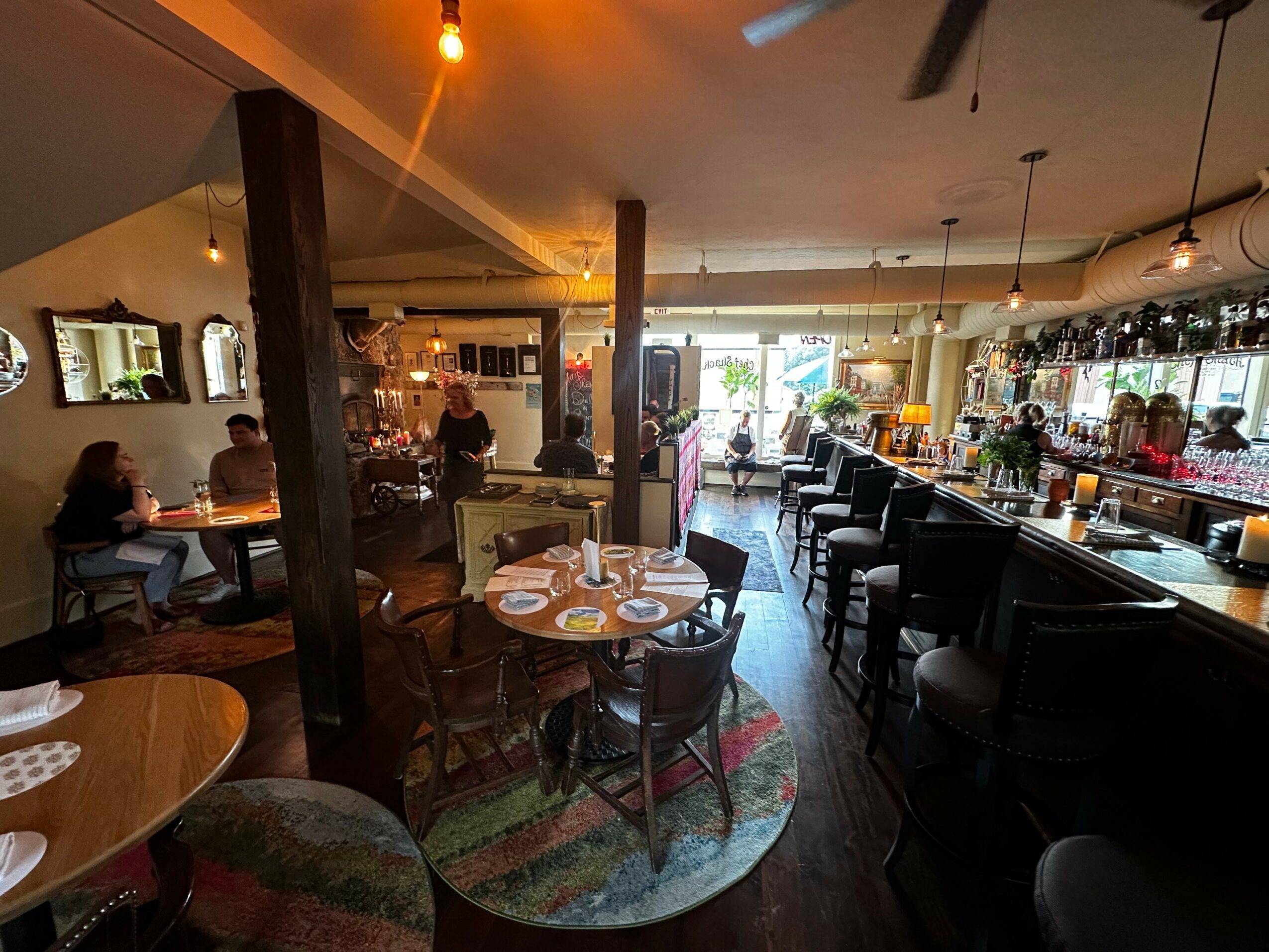 Interior of a cozy restaurant or cafe with tables, chairs, and a bar area, illuminated by warm lighting.