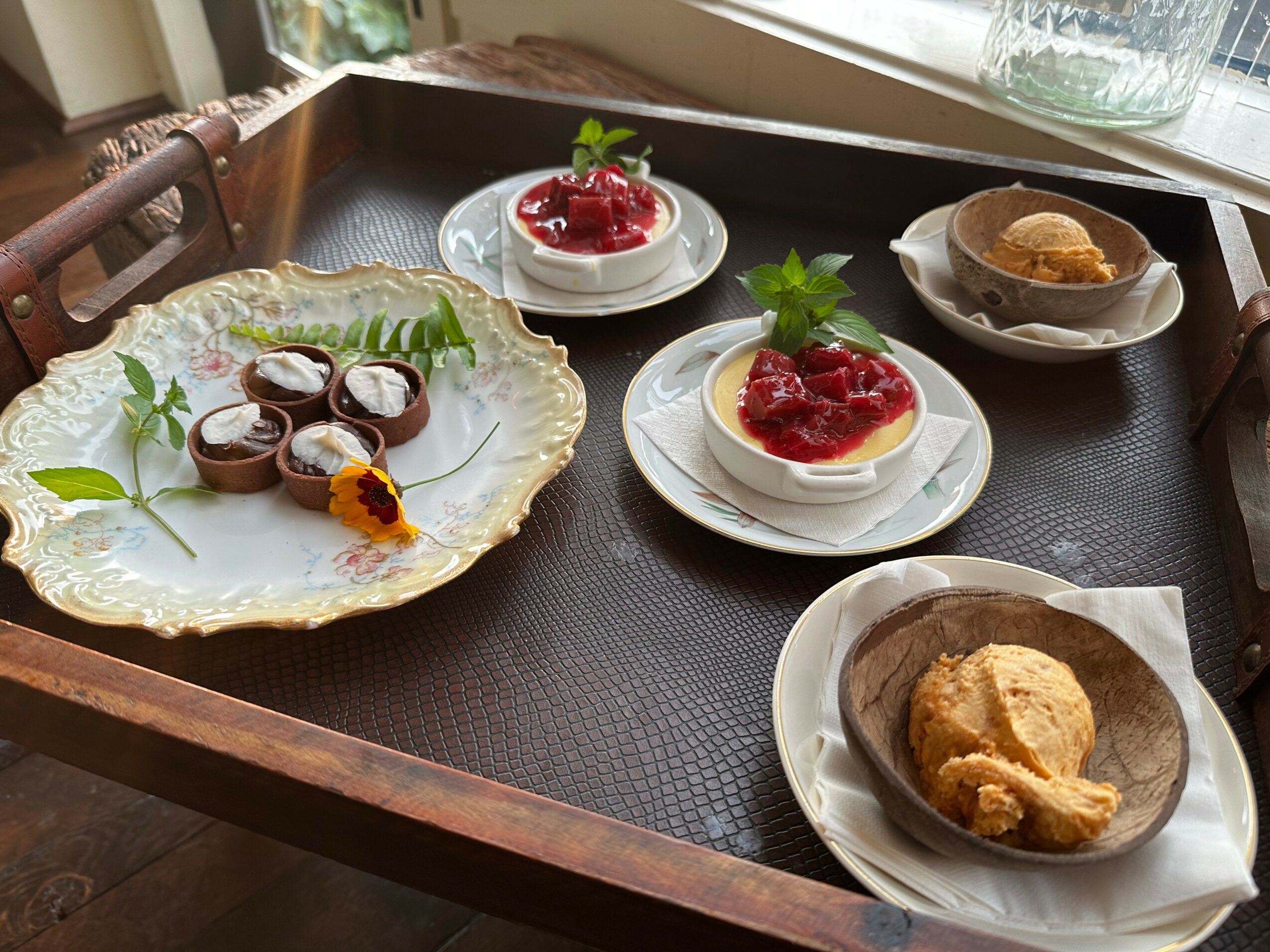 Assorted desserts on a tray, including chocolate, fruit, and cake, with a window in the background.