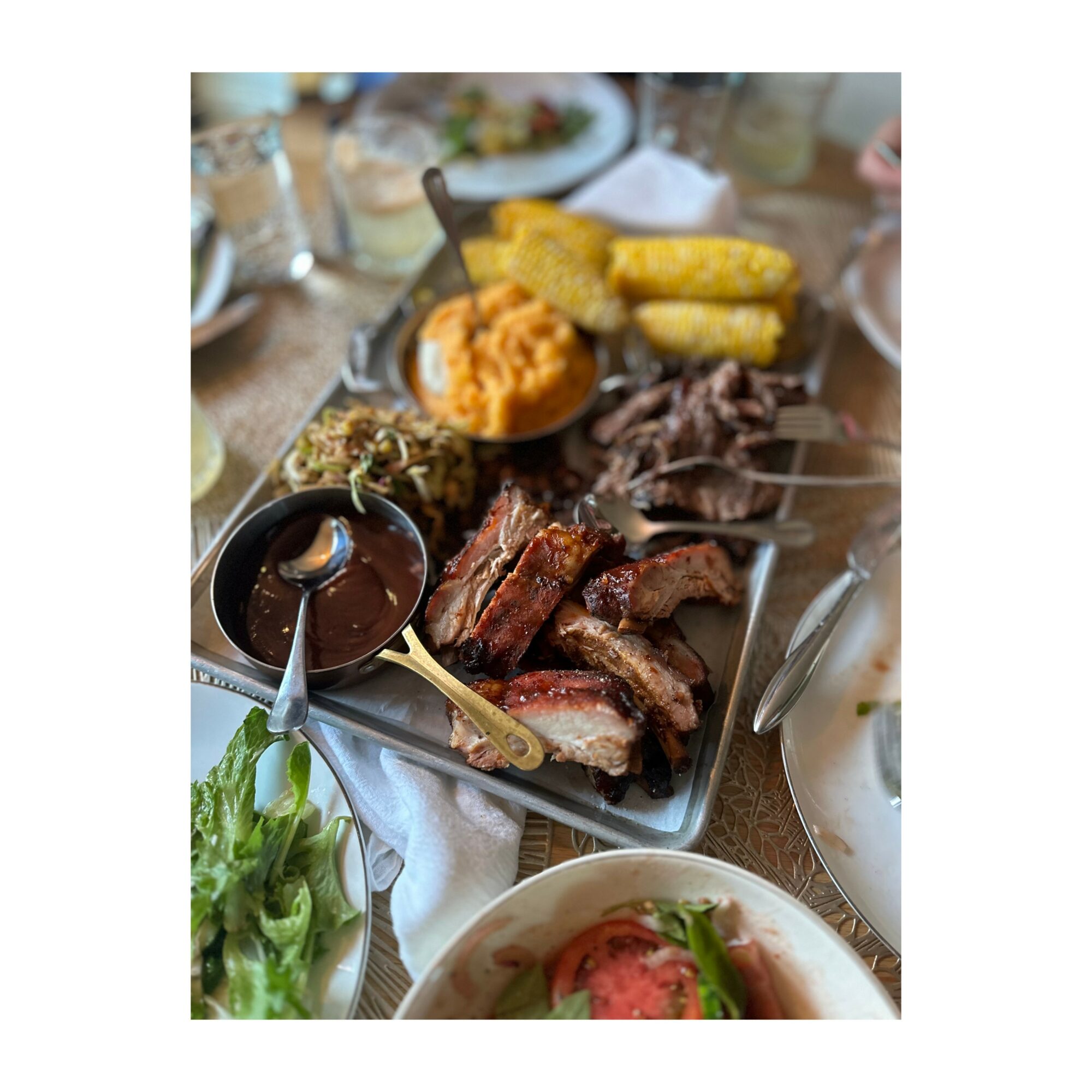 Assorted grilled meats, fried plantains, and side dishes on a table, with a salad in the foreground.