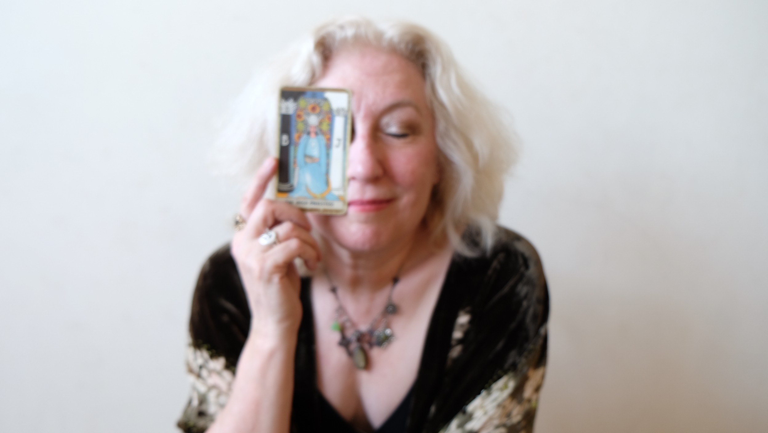 Woman with blonde hair holding a phone to her face, smiling, against a plain background.