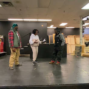 Three people standing on a stage in a store, with shelves and boxes in the background.