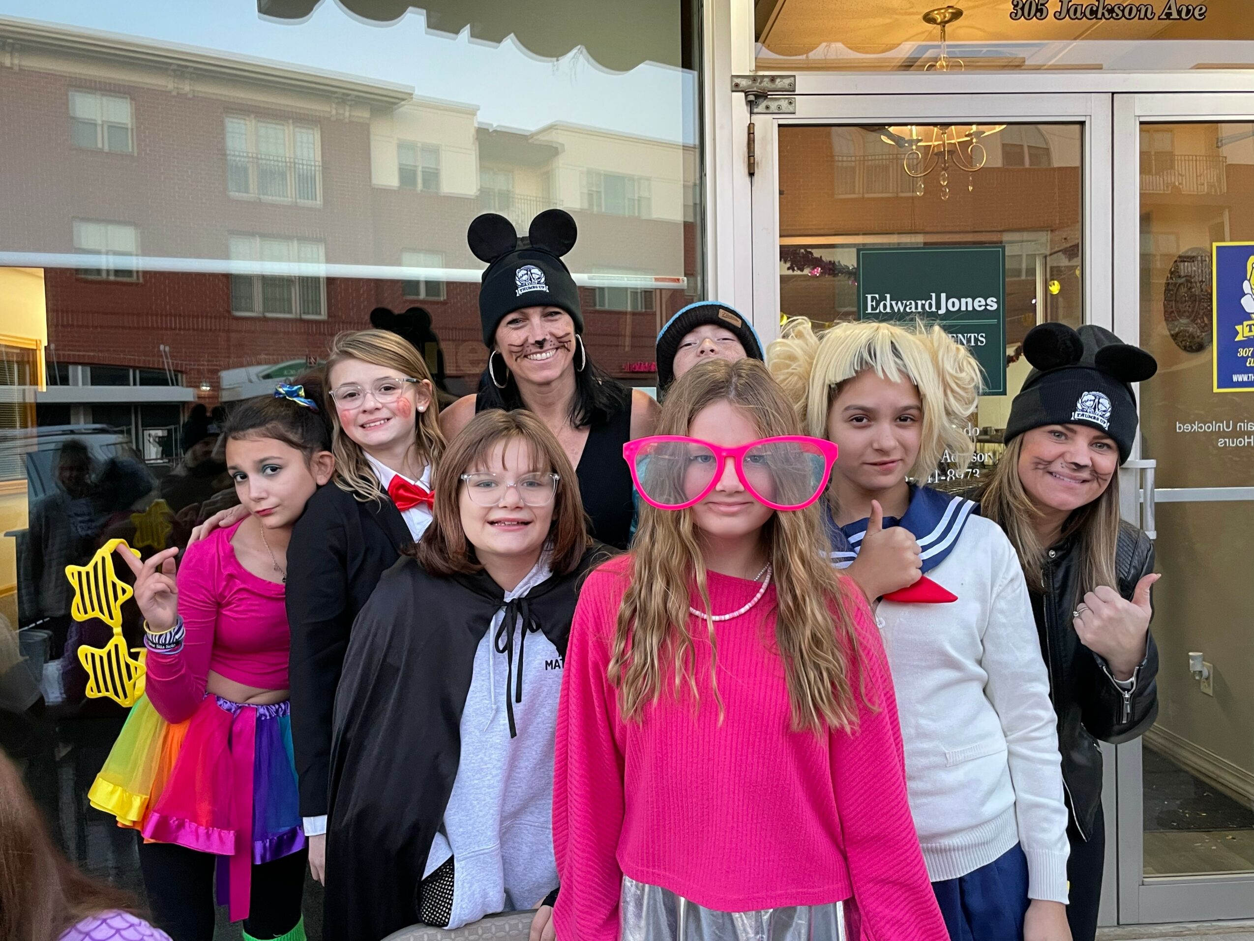 Group of children and teenagers wearing Mickey Mouse ears and colorful clothing outside a store.