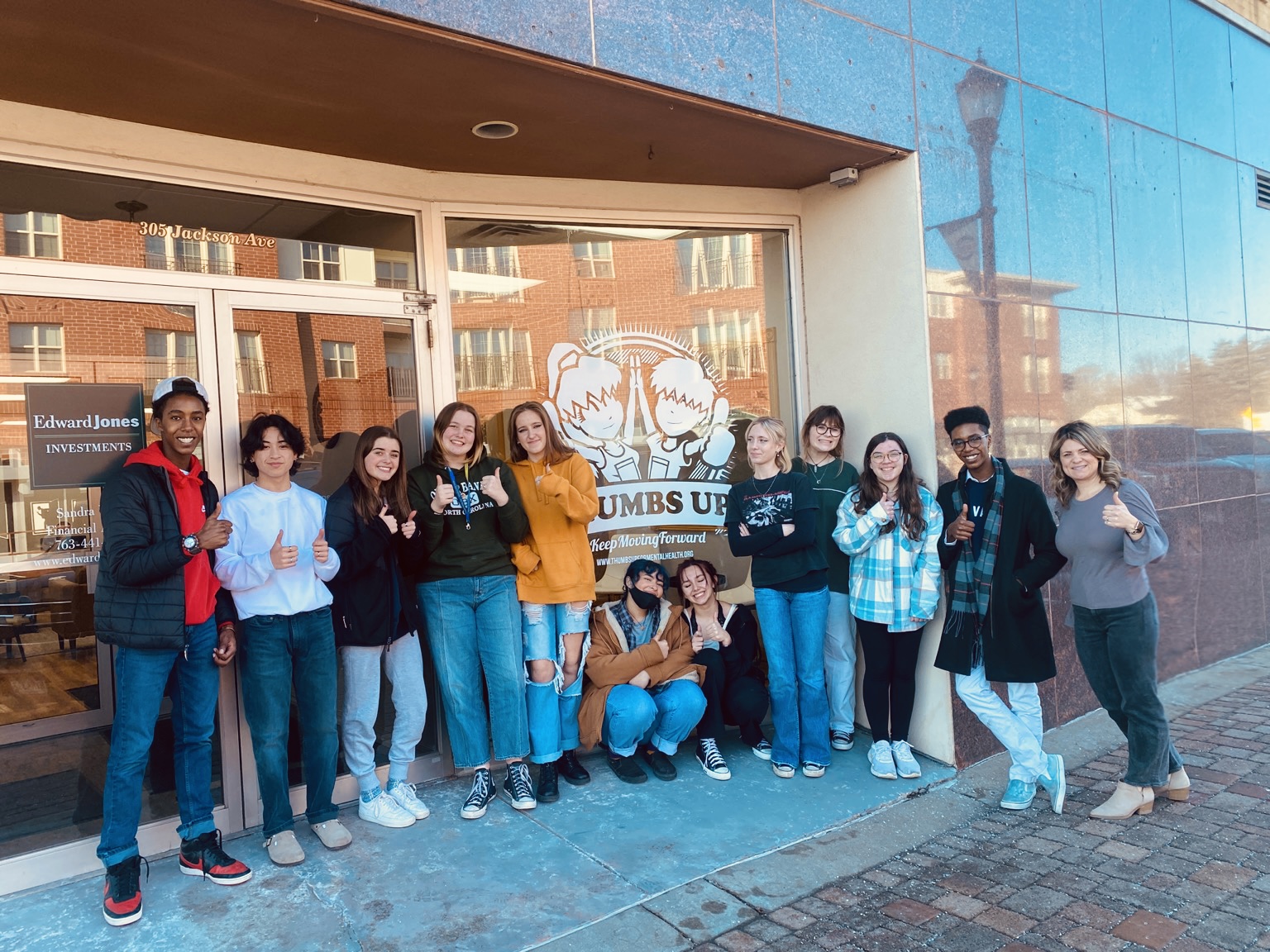 Group of ten people standing outside a building, smiling, with a large logo on the window behind them.