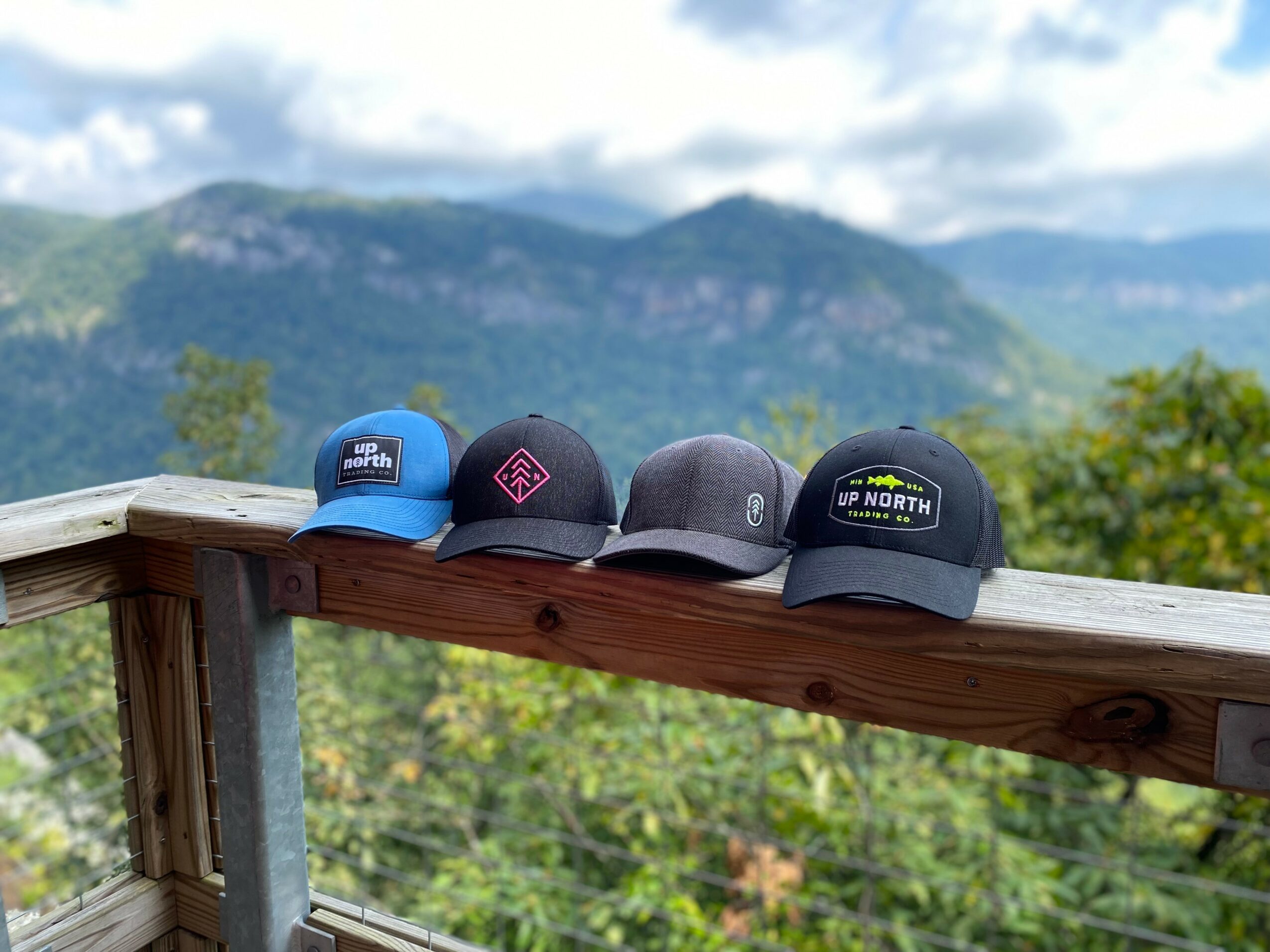 Four hats placed on a wooden railing with a mountain landscape in the background.