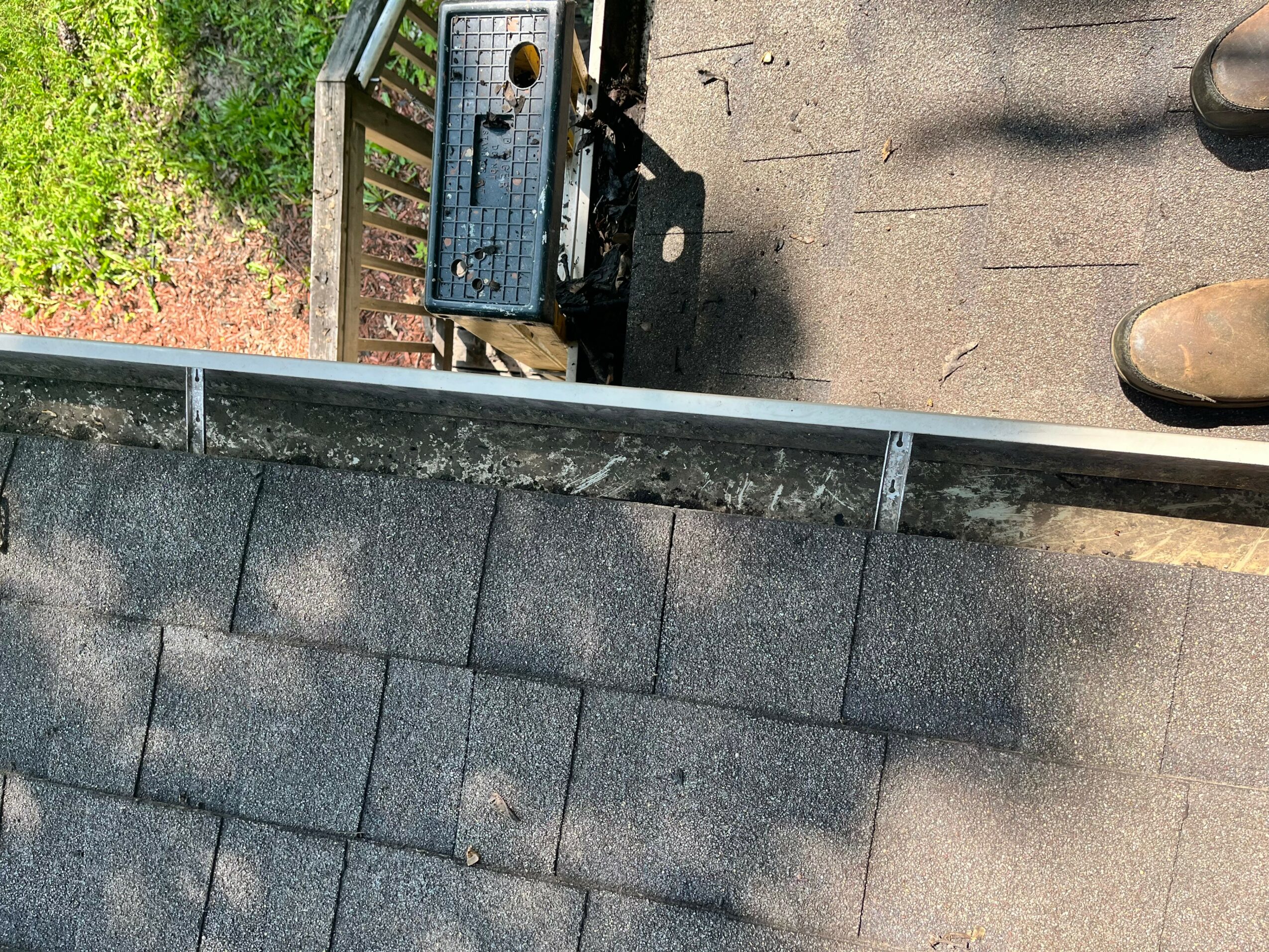 View from above of a rooftop with shingles, a bench, and shoes on the ground, with trees in the background.