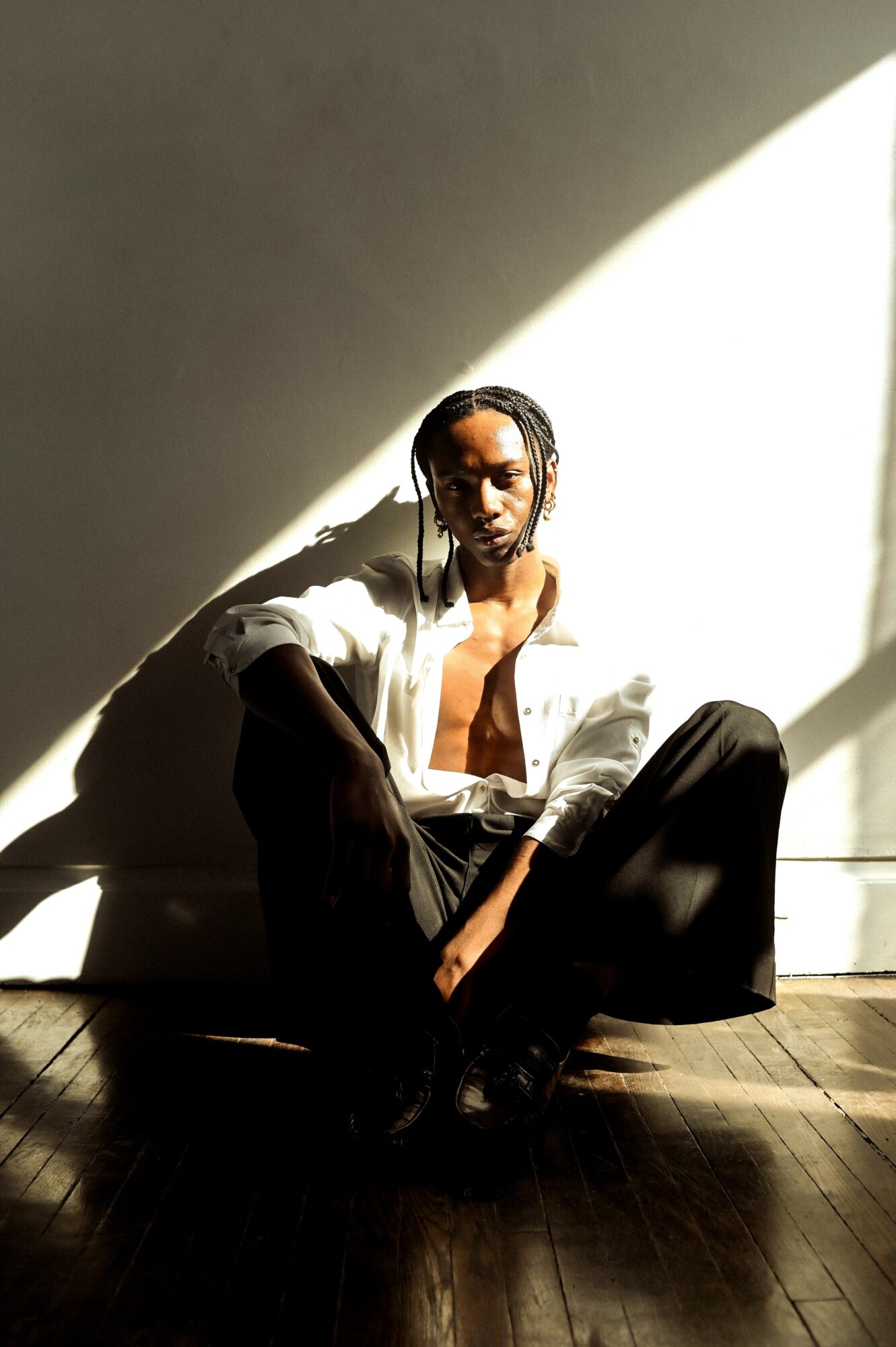 Person sitting on the floor with legs crossed, illuminated by sunlight, against a plain wall background.
