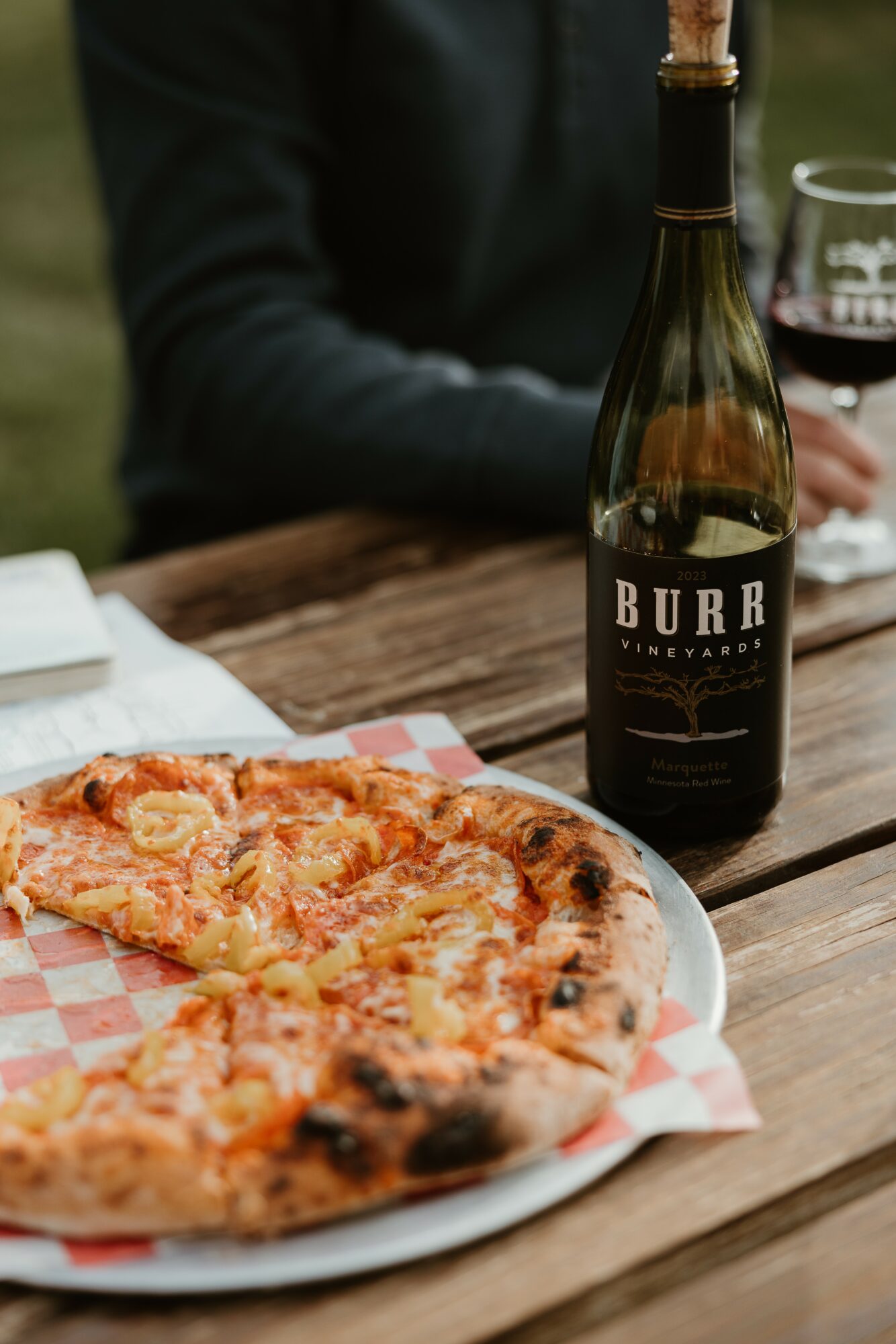 Pizza on a plate with a bottle of wine and a glass in the background, on a wooden table.