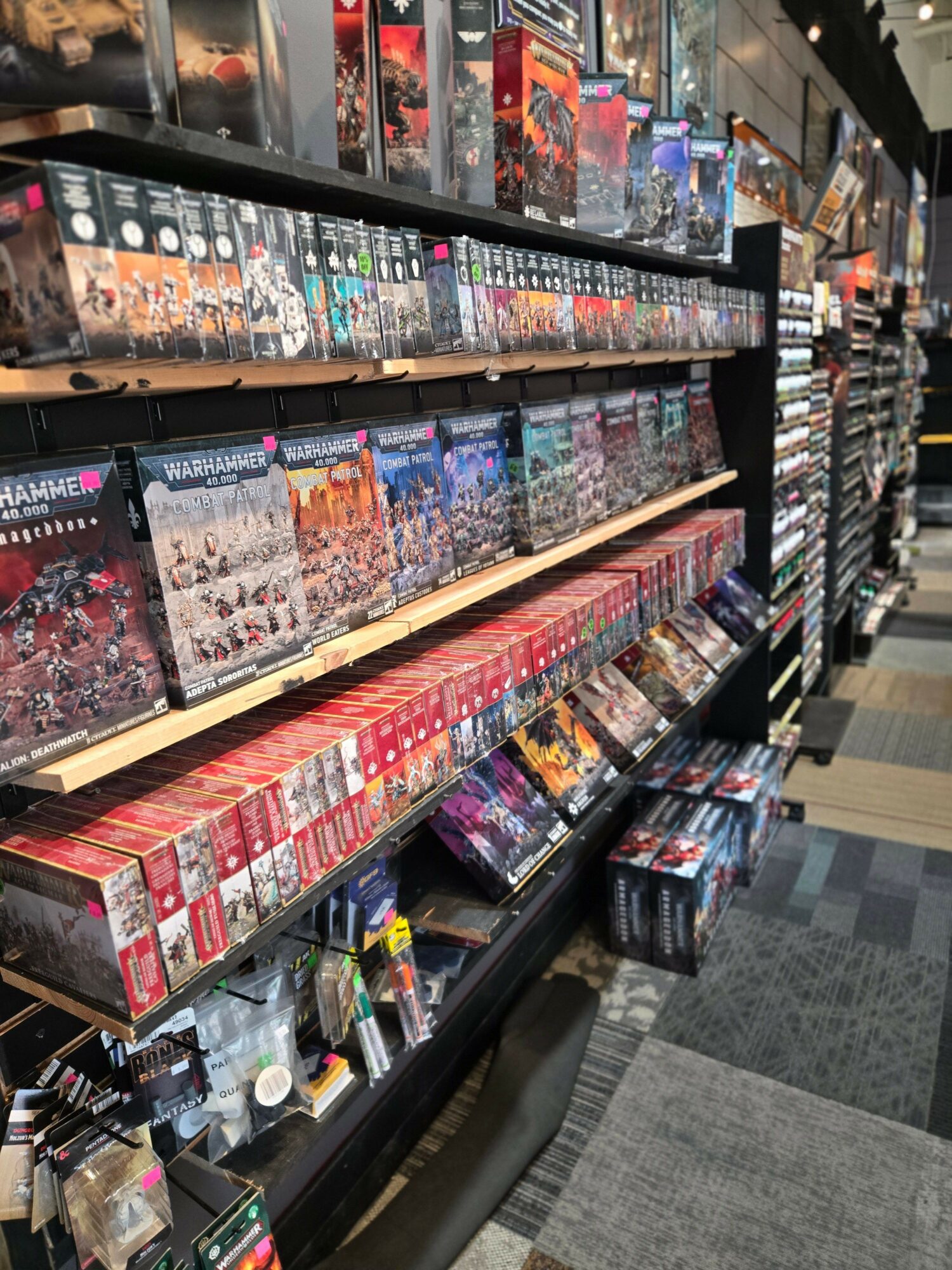 Table with numerous board game boxes and gaming accessories arranged in rows, in a room with gray walls.