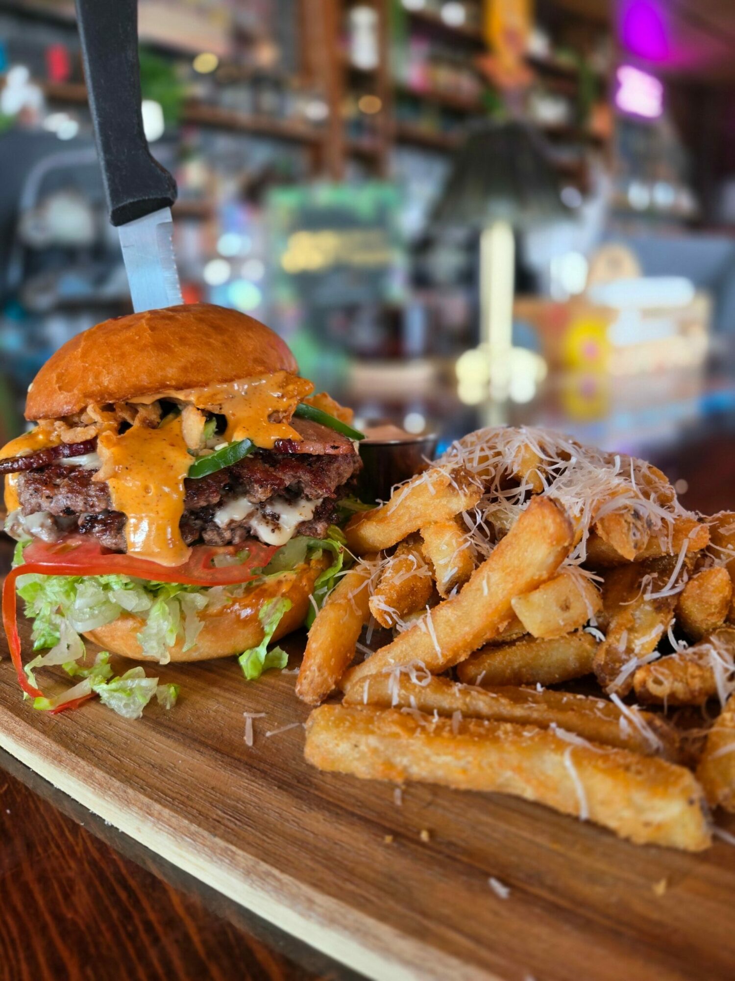 Fried cheese sticks and a burger with lettuce, tomato, cheese, and a bun on a wooden board.