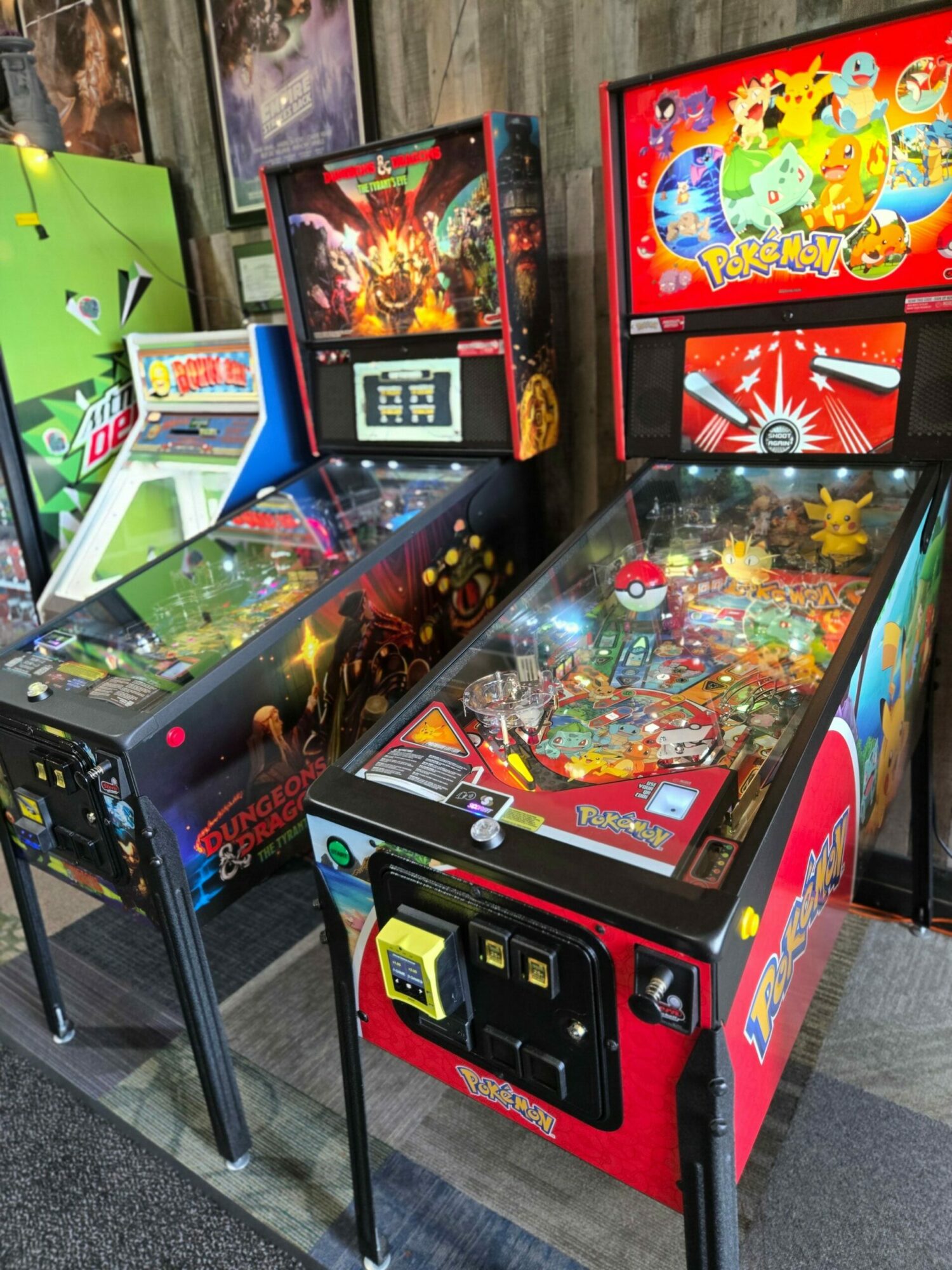 Three pinball machines with colorful artwork and digital displays, placed side by side on a gray floor.
