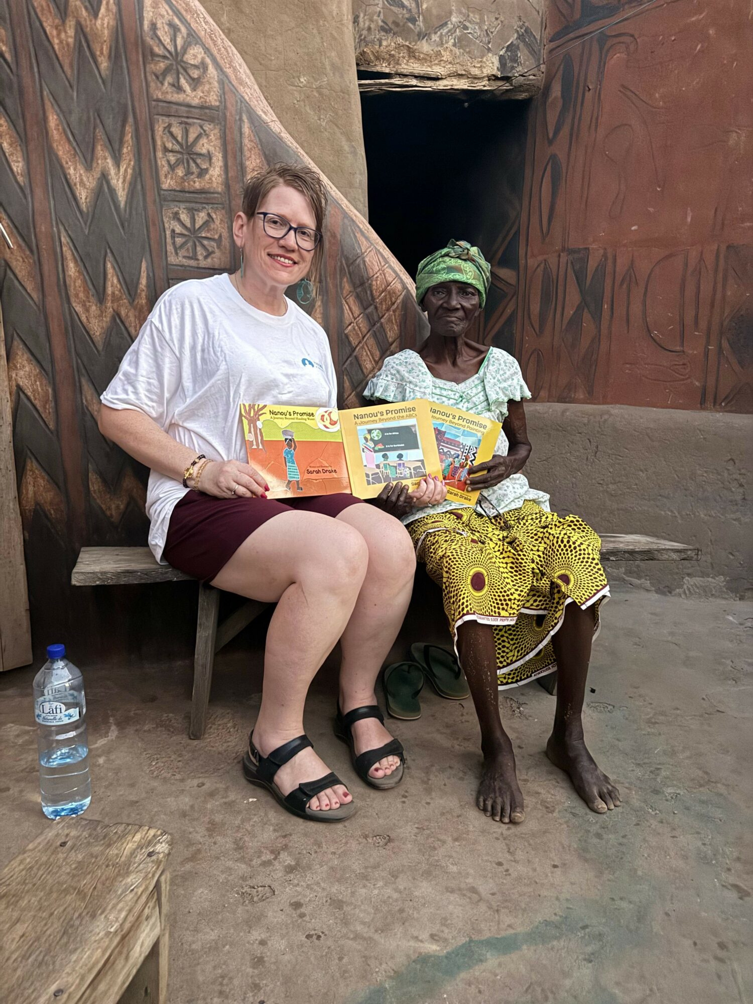 Woman sitting on a chair reading a book, with a child standing behind her, in a rustic setting.