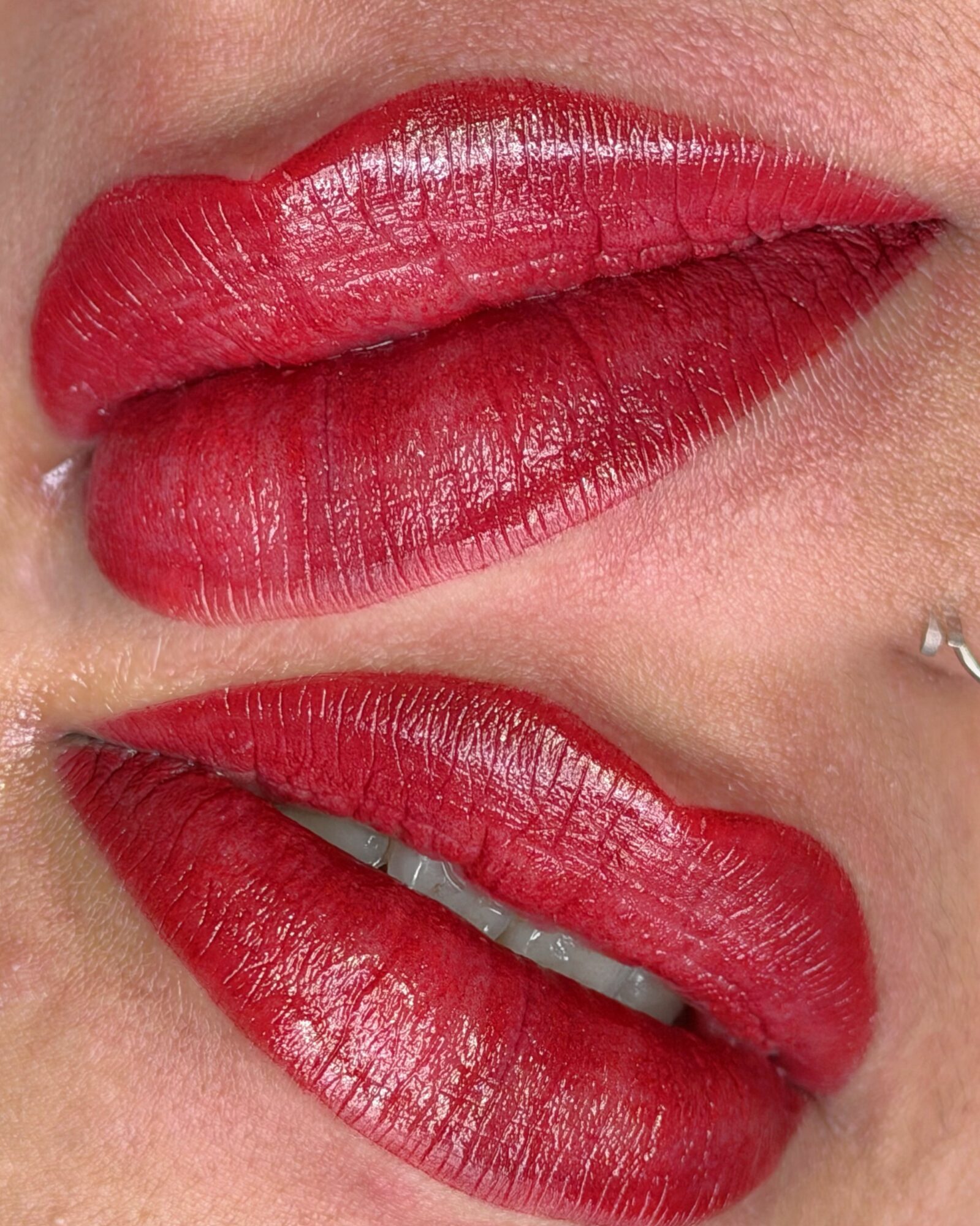 Close-up of lips with red lipstick, slightly parted showing teeth, skin visible around lips.