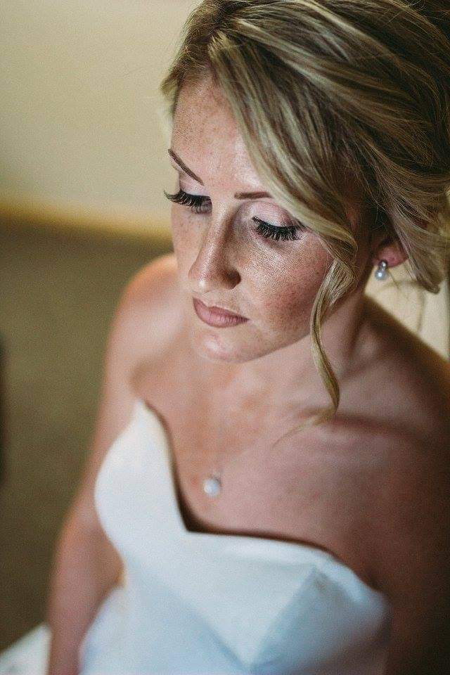 Close-up of a woman with styled hair and makeup, wearing a strapless white dress, looking downward.