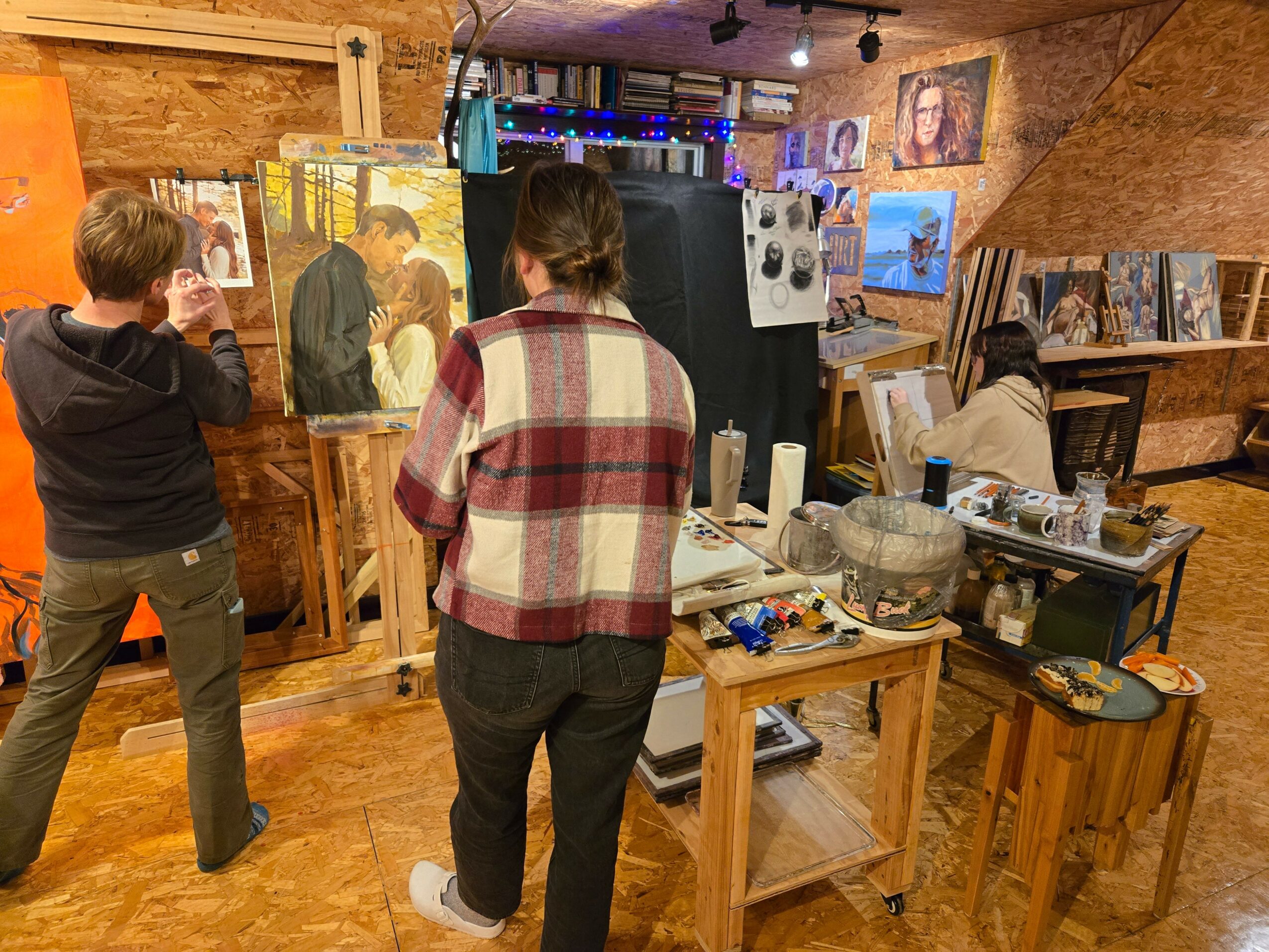 People viewing artwork and photographs in an art gallery with wooden walls and display tables.