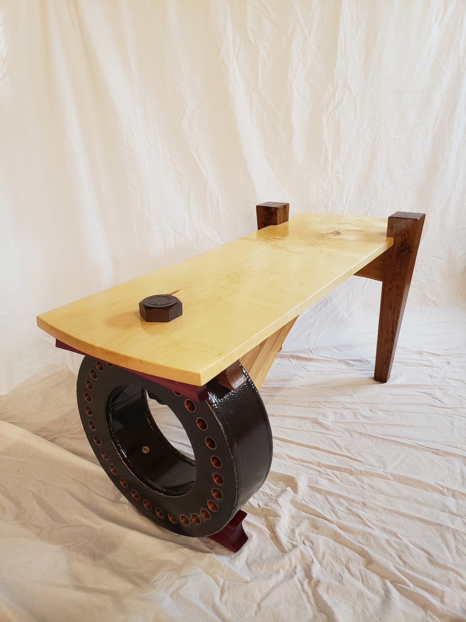 Wooden table with a large black circular metal base, set against a white fabric background.
